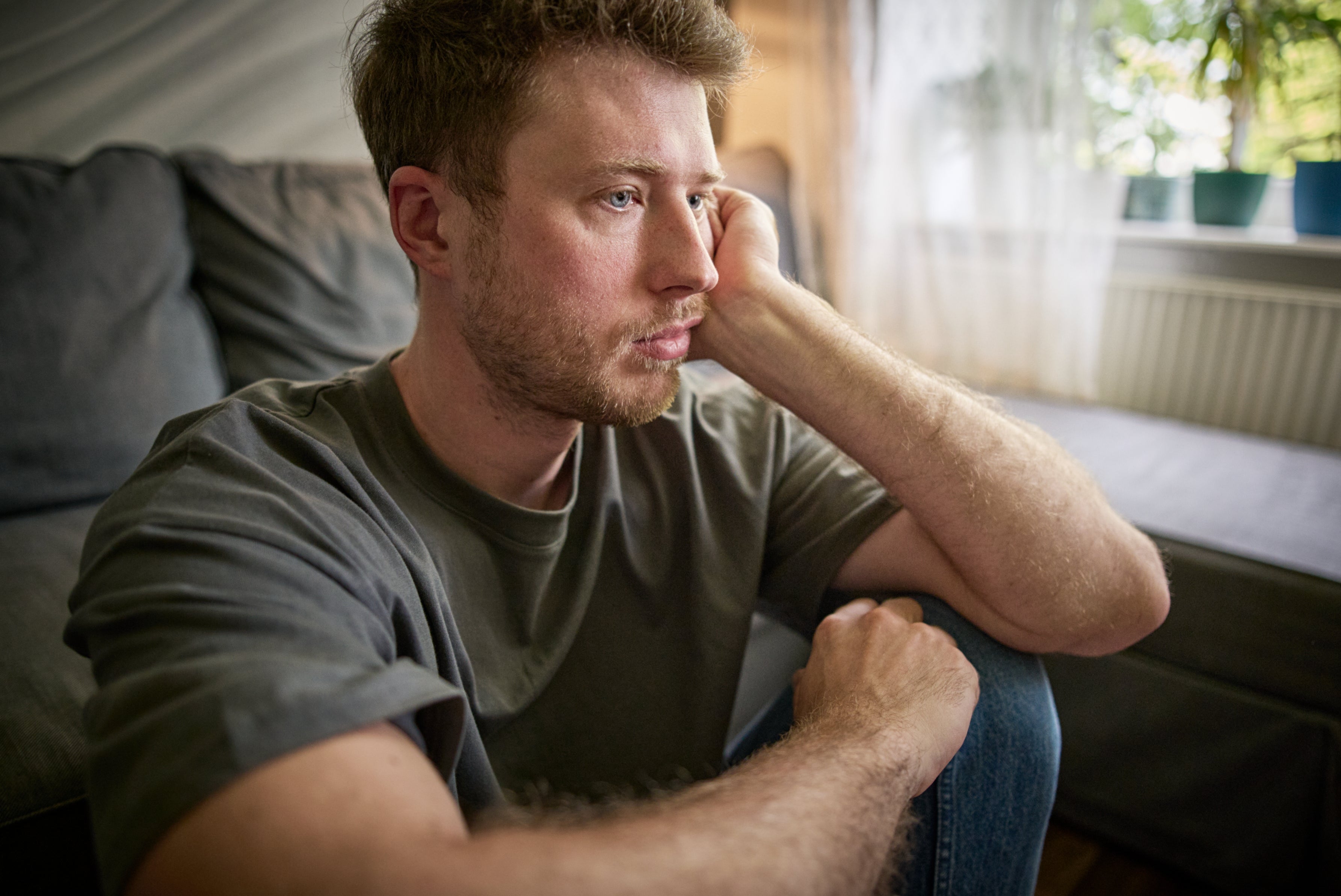 Person with abbreviated  hairsbreadth  sits pensively connected  a couch, resting a manus  connected  their face, looking distant   and thoughtful successful  a surviving  country   setting
