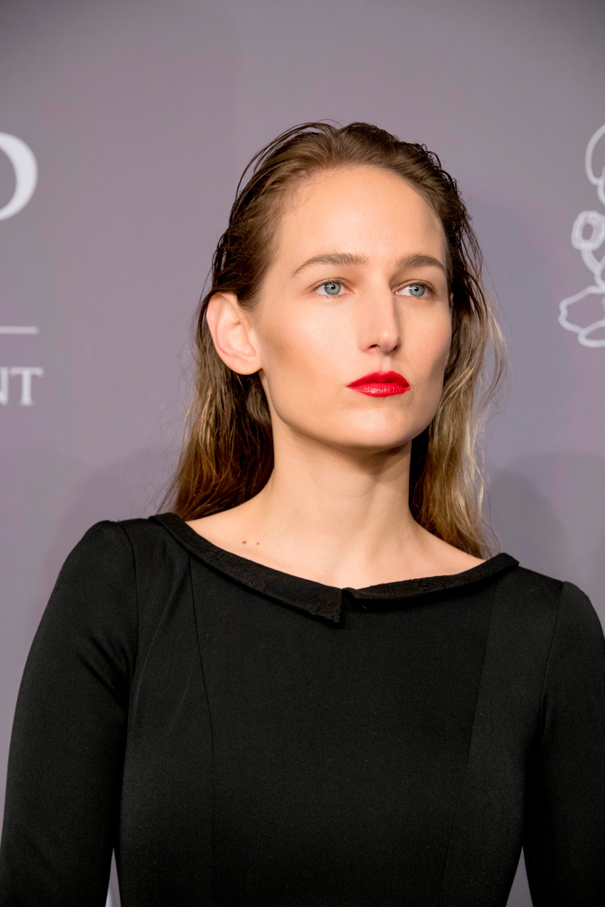 Person on red carpet in sleek black dress with wet look hairstyle and bold lipstick