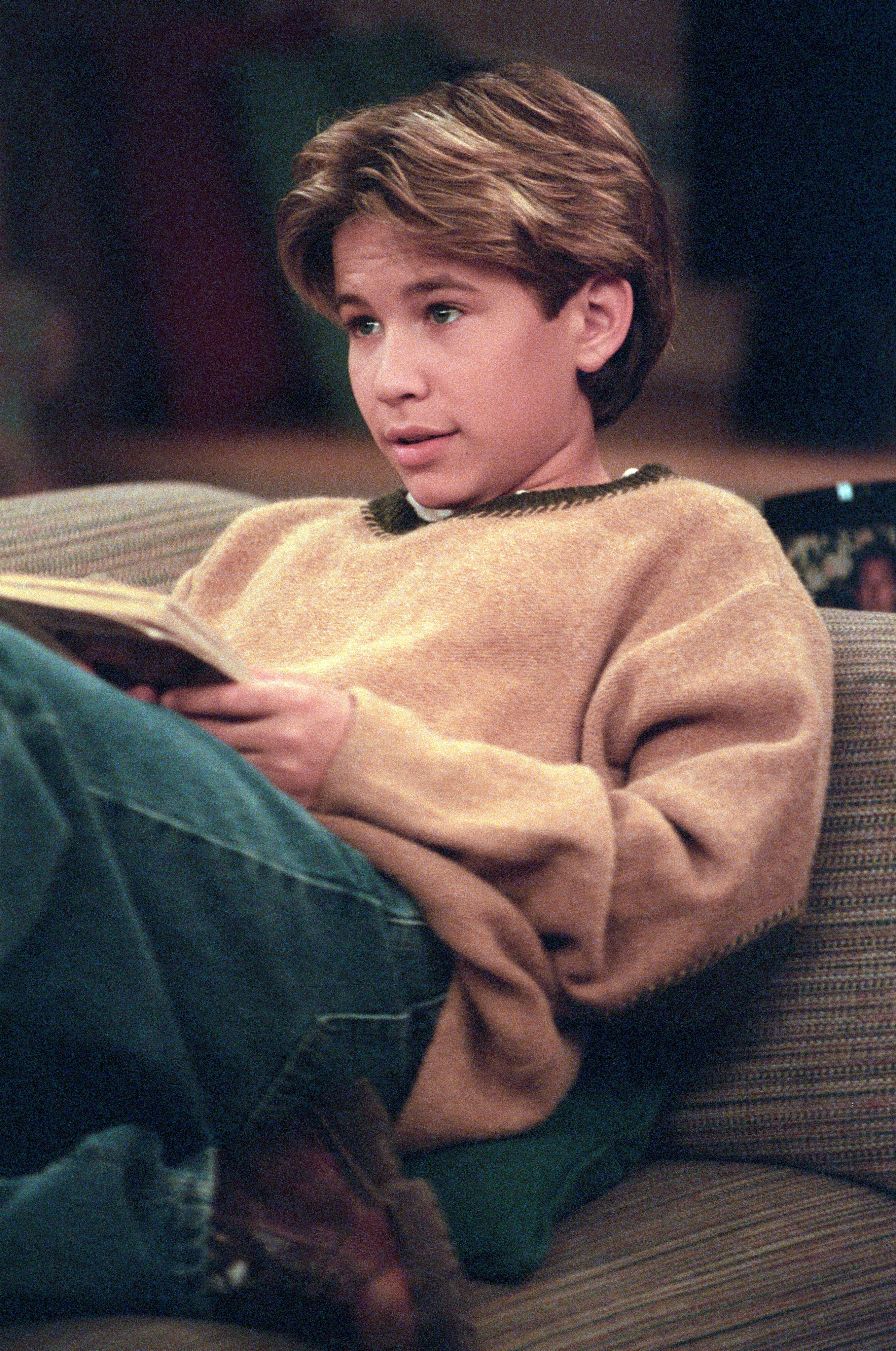 Person lounging on a couch, reading a book, dressed casually in a sweater and jeans