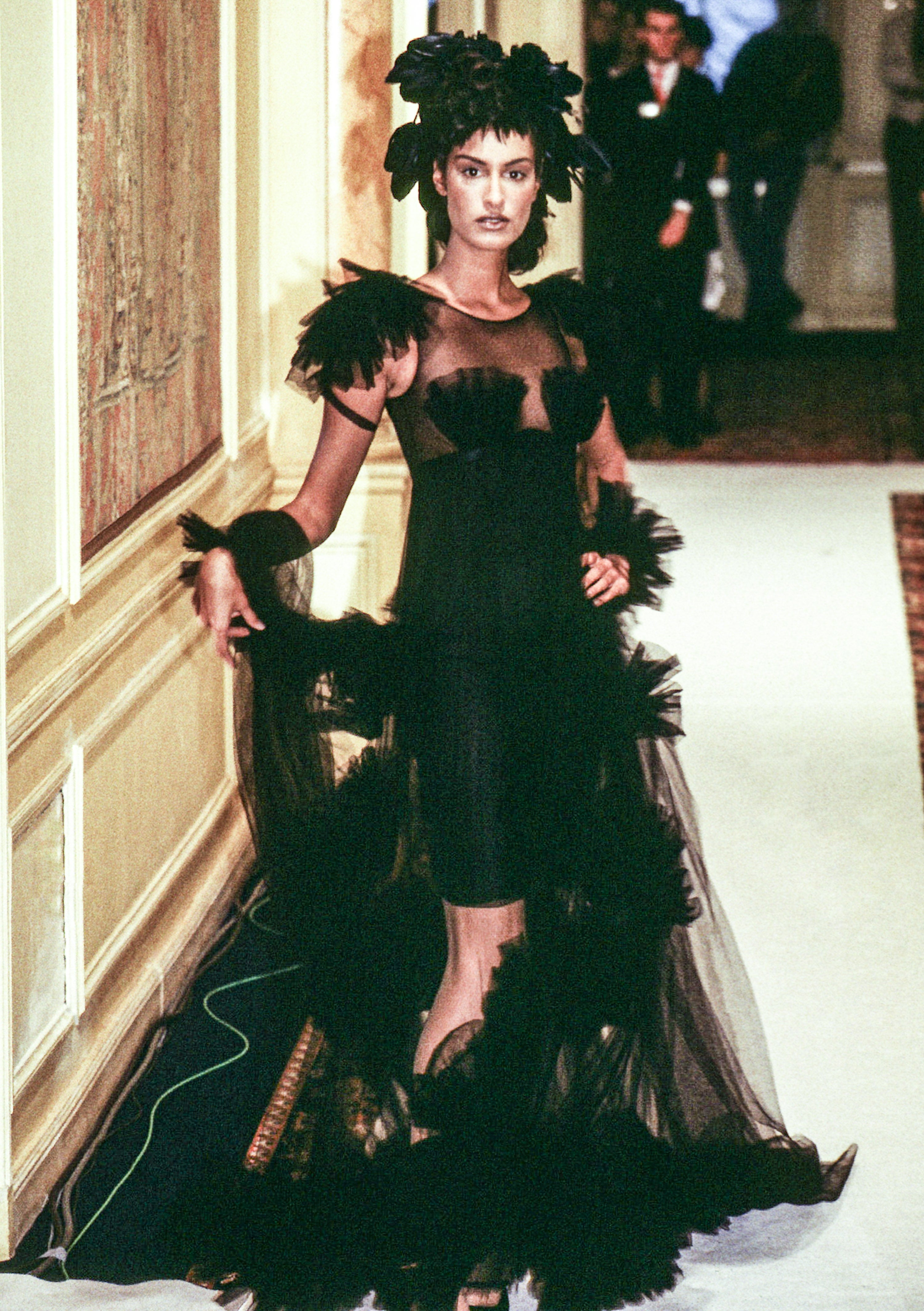 Person in a sheer black dress with feather details on a runway, exuding elegance and style