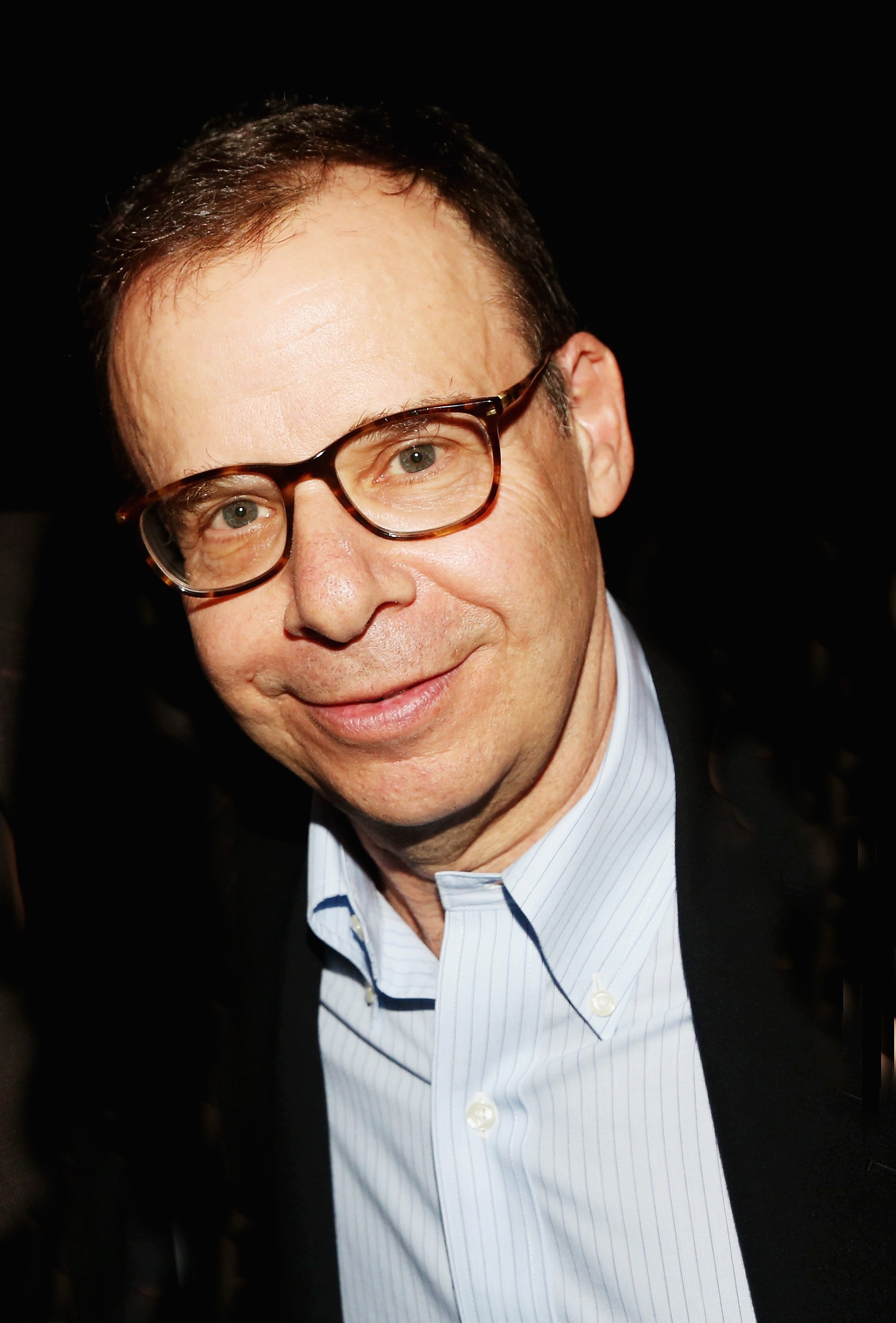 A smiling person with glasses in a suit jacket and a striped shirt