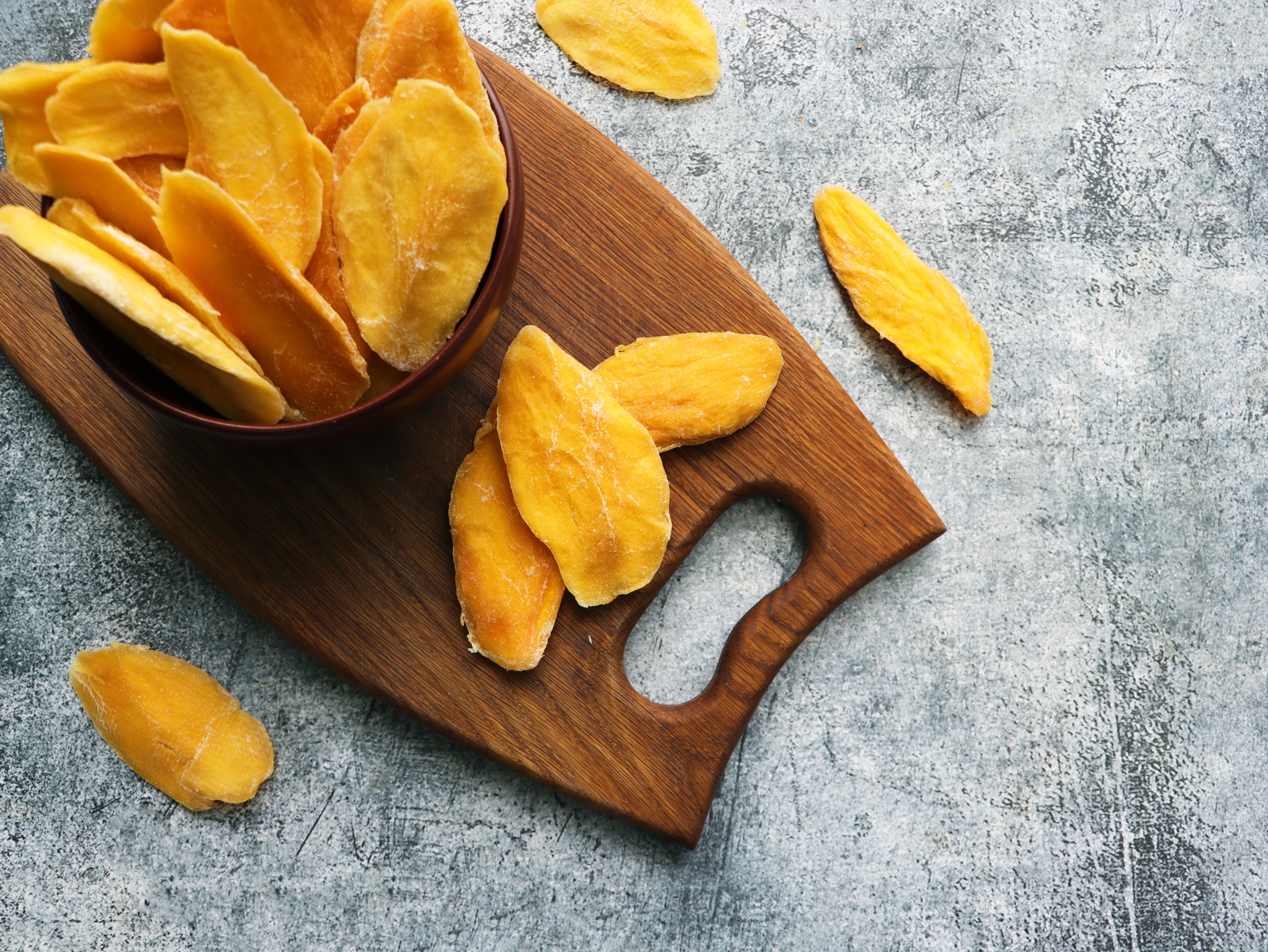 Dried mango slices successful  a vessel  connected  a woody  board, scattered crossed  a textured surface