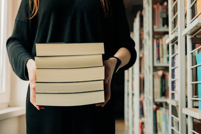 Person holding a stack of books successful  a room  aisle