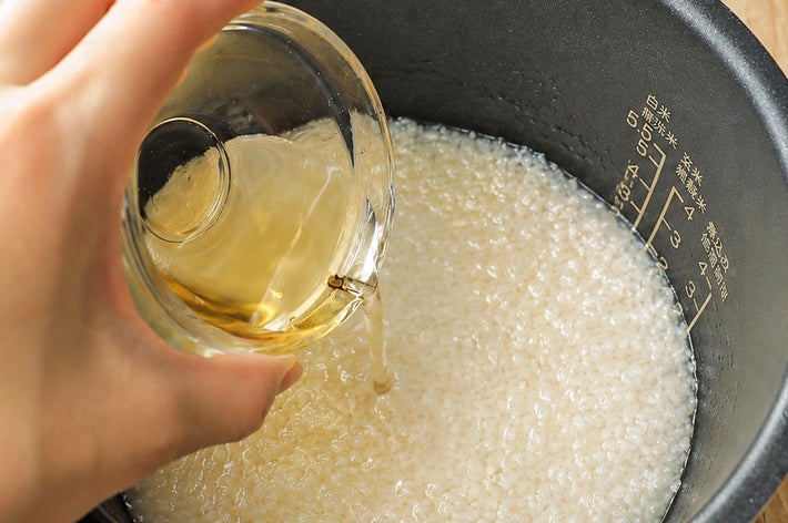 炊飯器の中にお米と水が入っており、手が追加の液体を注いでいる様子。
