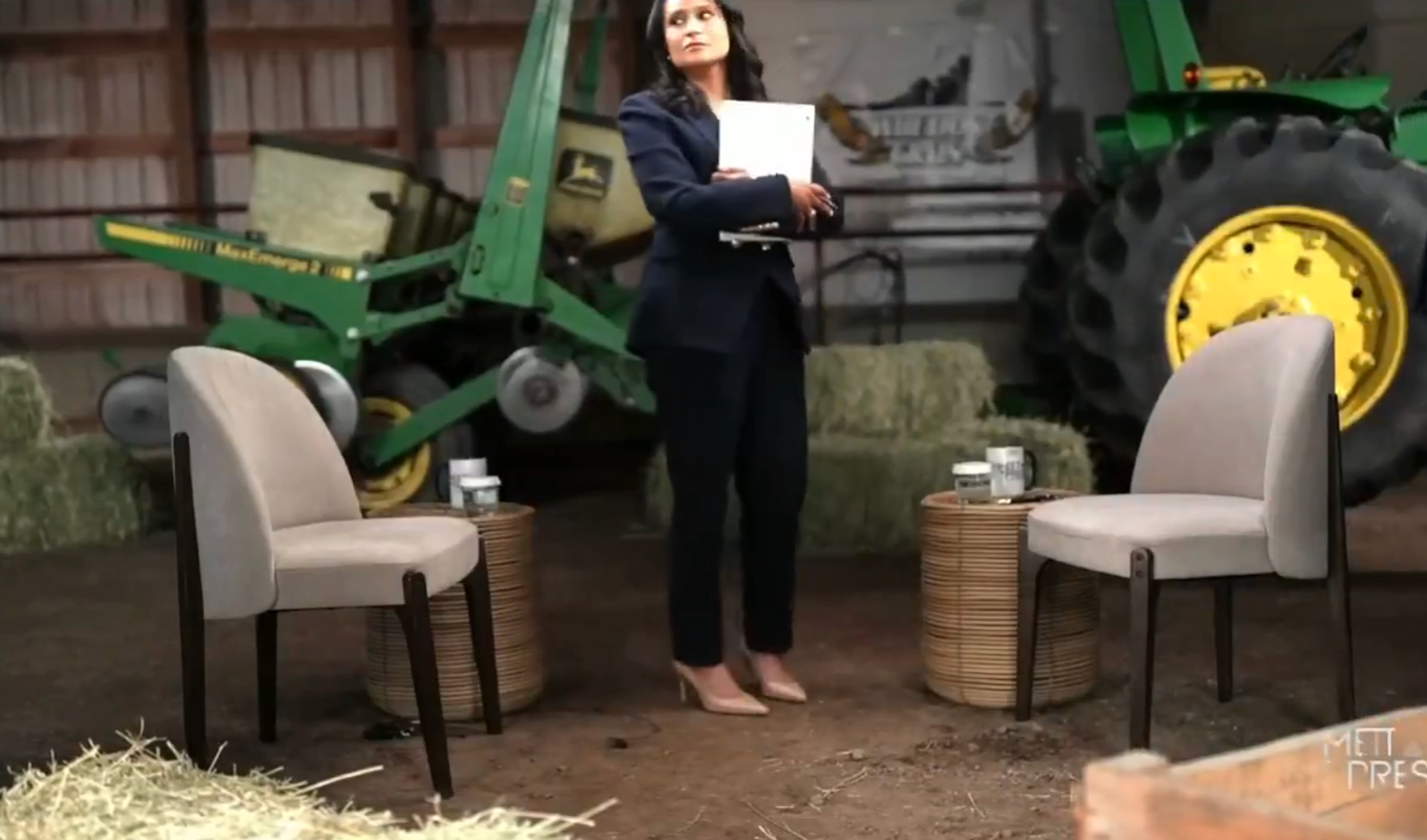 A idiosyncratic successful a suit stands successful a barn with hay bales, chairs, and workplace equipment, holding a document, perchance preparing for an interrogation oregon event