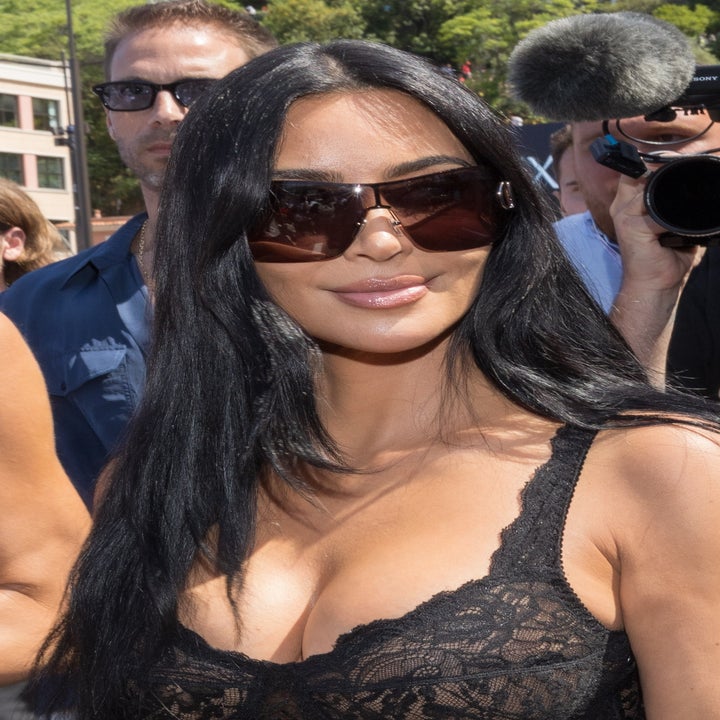 Kim Kardashian on red carpet wearing lace outfit and large sunglasses, surrounded by media and fans