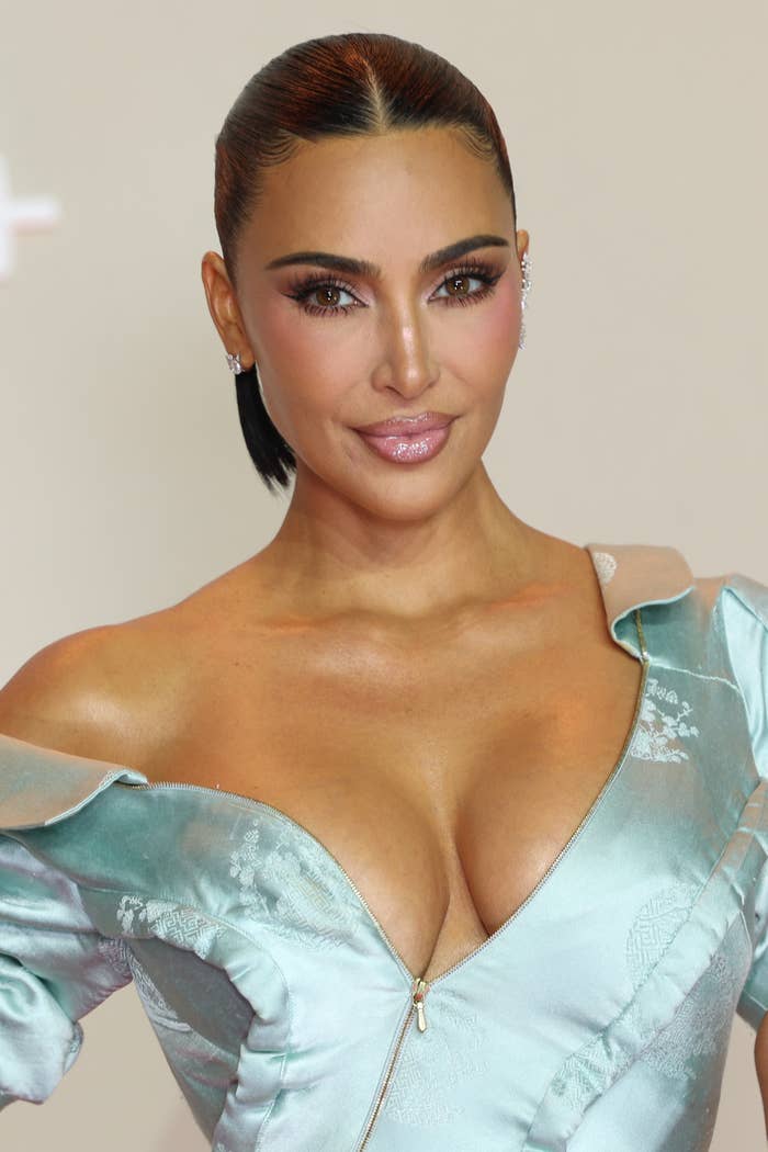 Kim Kardashian wearing an elegant, off-shoulder gown with intricate details, posing confidently at a celebrity event