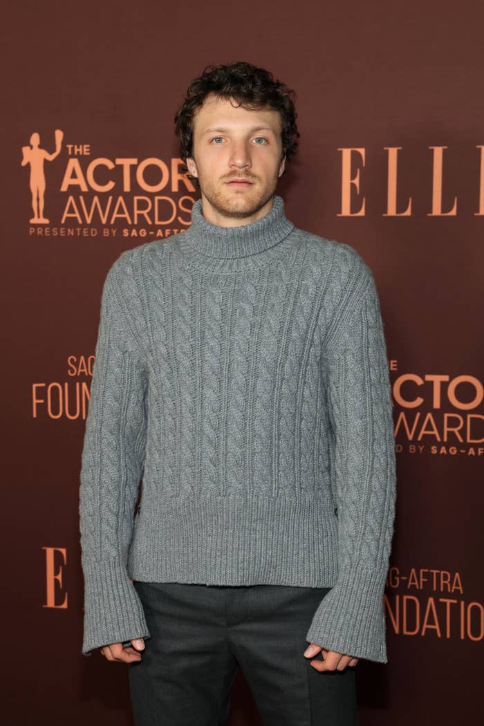 Person wearing a gray cable-knit turtleneck sweater and dark pants at an awards event