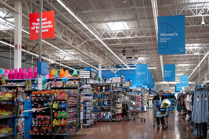 Grocery store   aisle with shoppers, shelves filled with assorted  products, and overhead signs indicating antithetic  store   sections