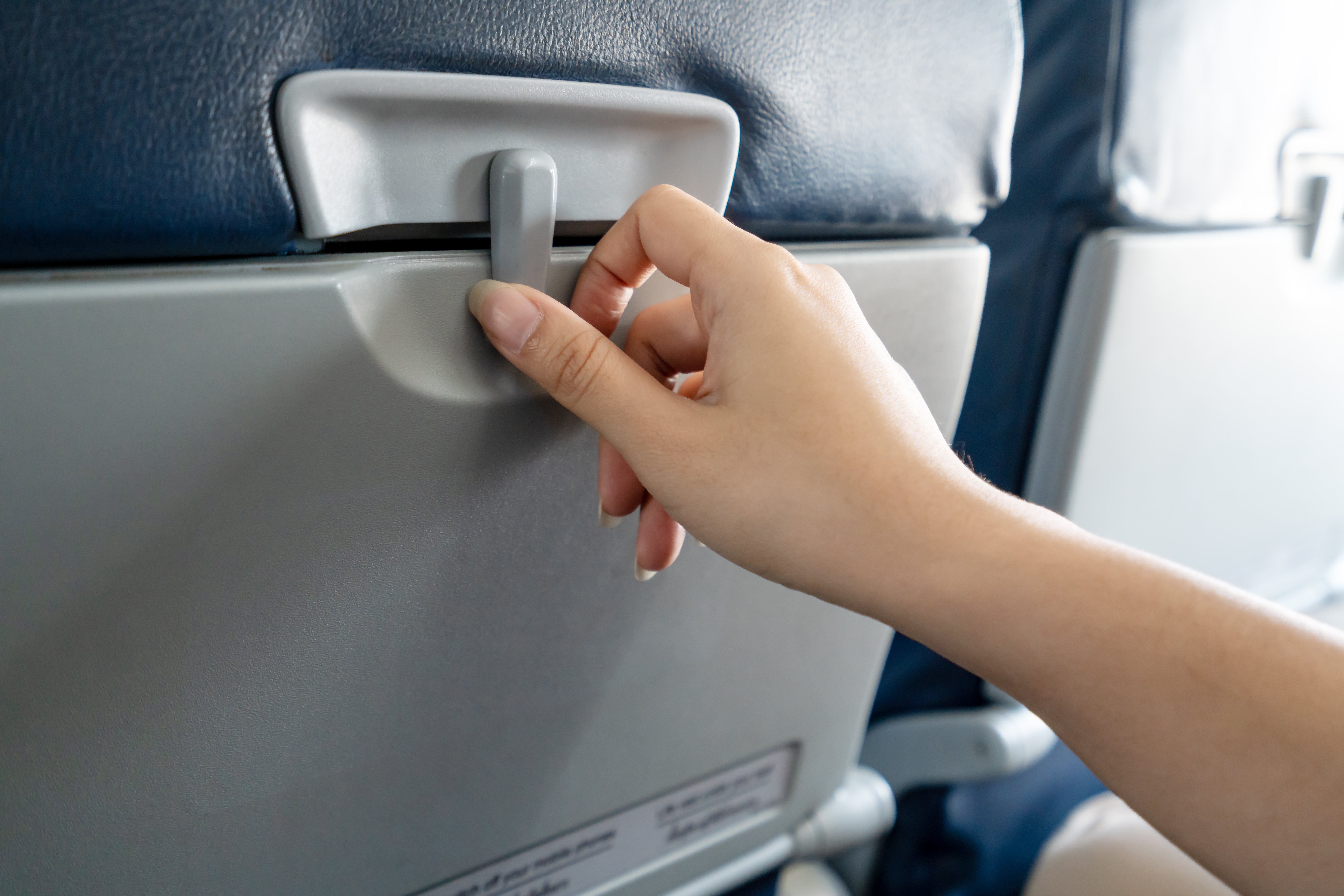 A hand adjusts a plane seat's tray table latch, preparing it for use