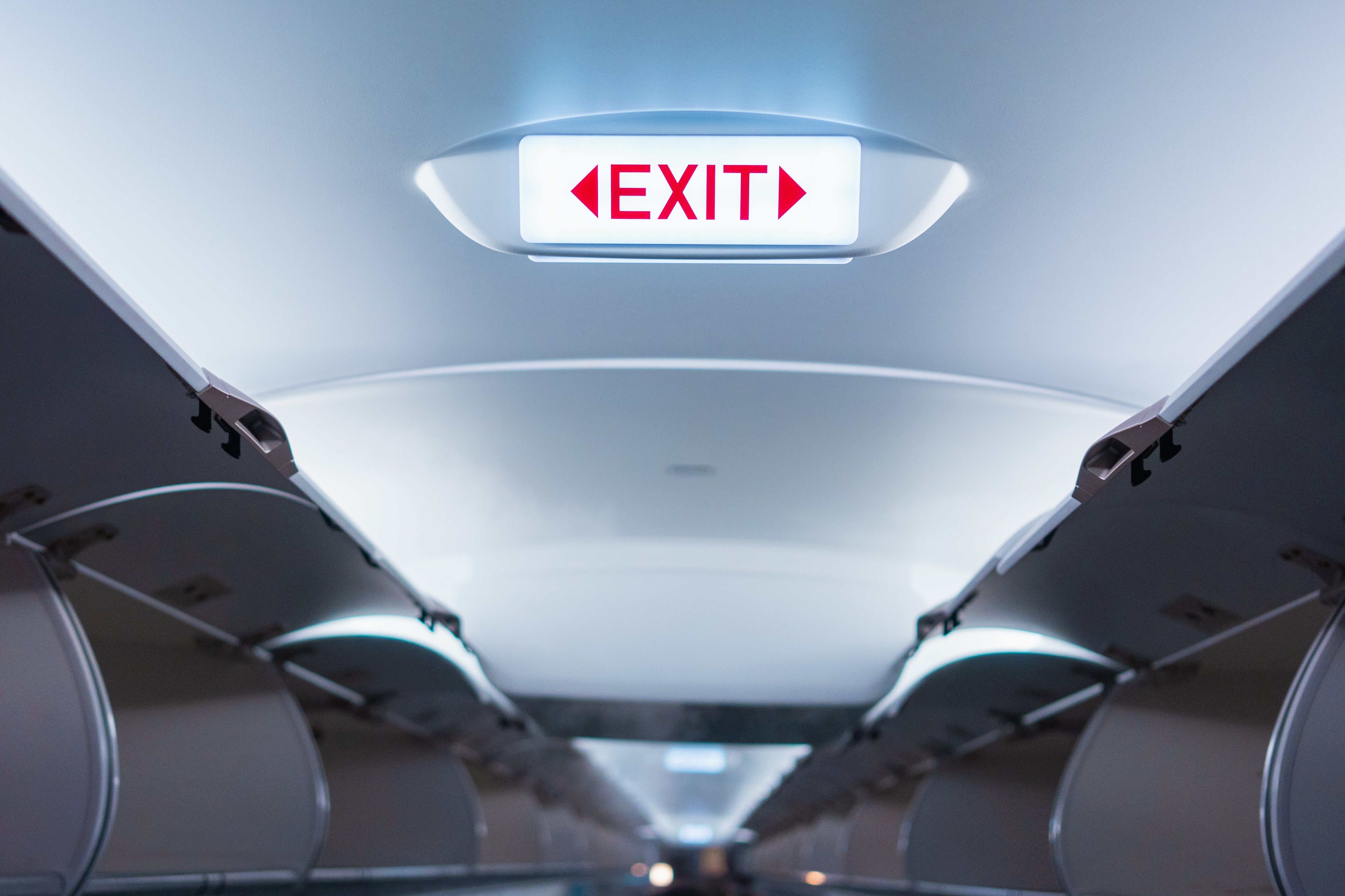 Airplane cabin view with illuminated "EXIT" sign and overhead storage compartments