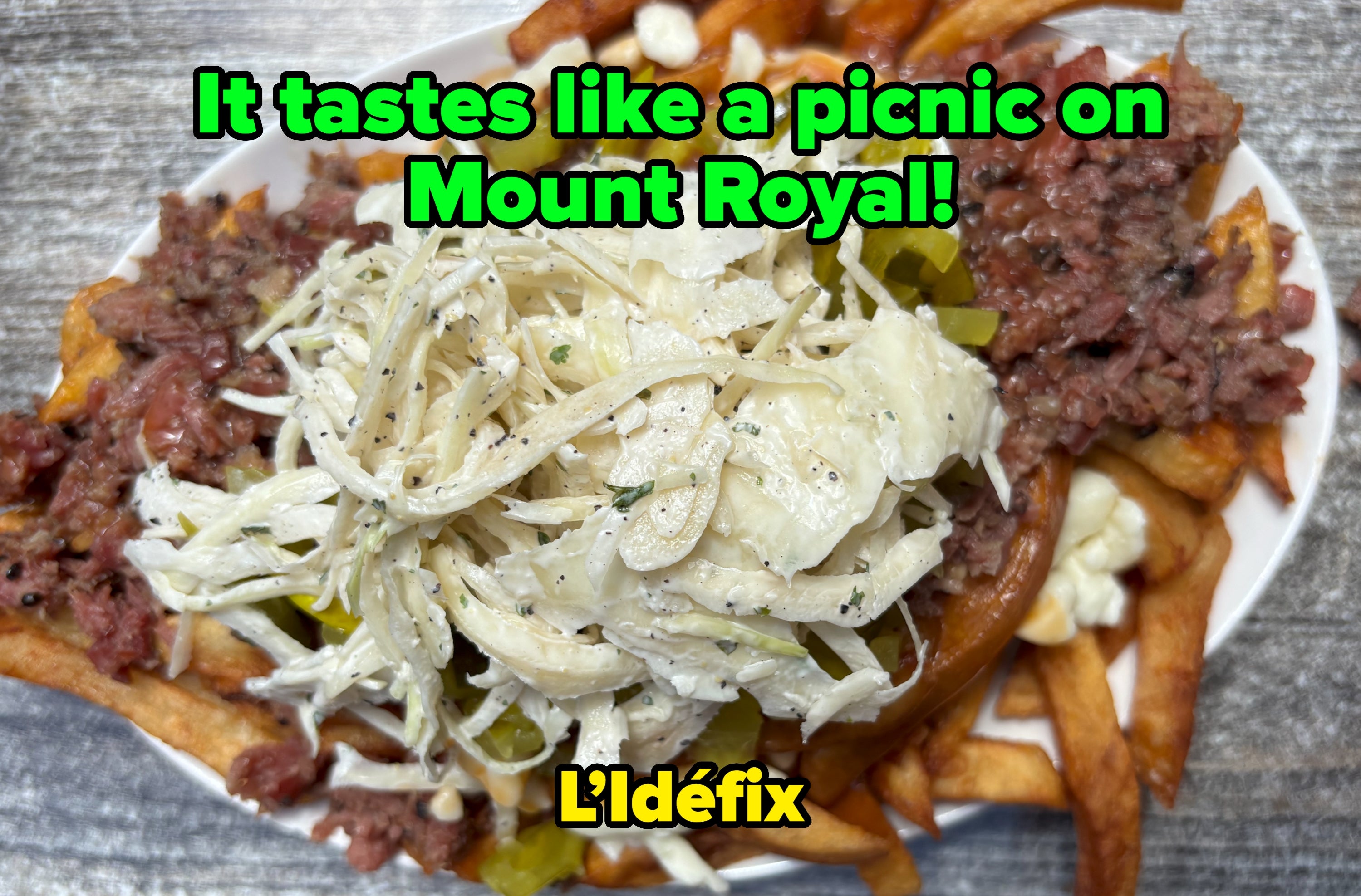 A sheet of loaded fries topped with sliced beef, shredded cabbage, pickles, and a creamy dressing, presented connected a rustic woody table