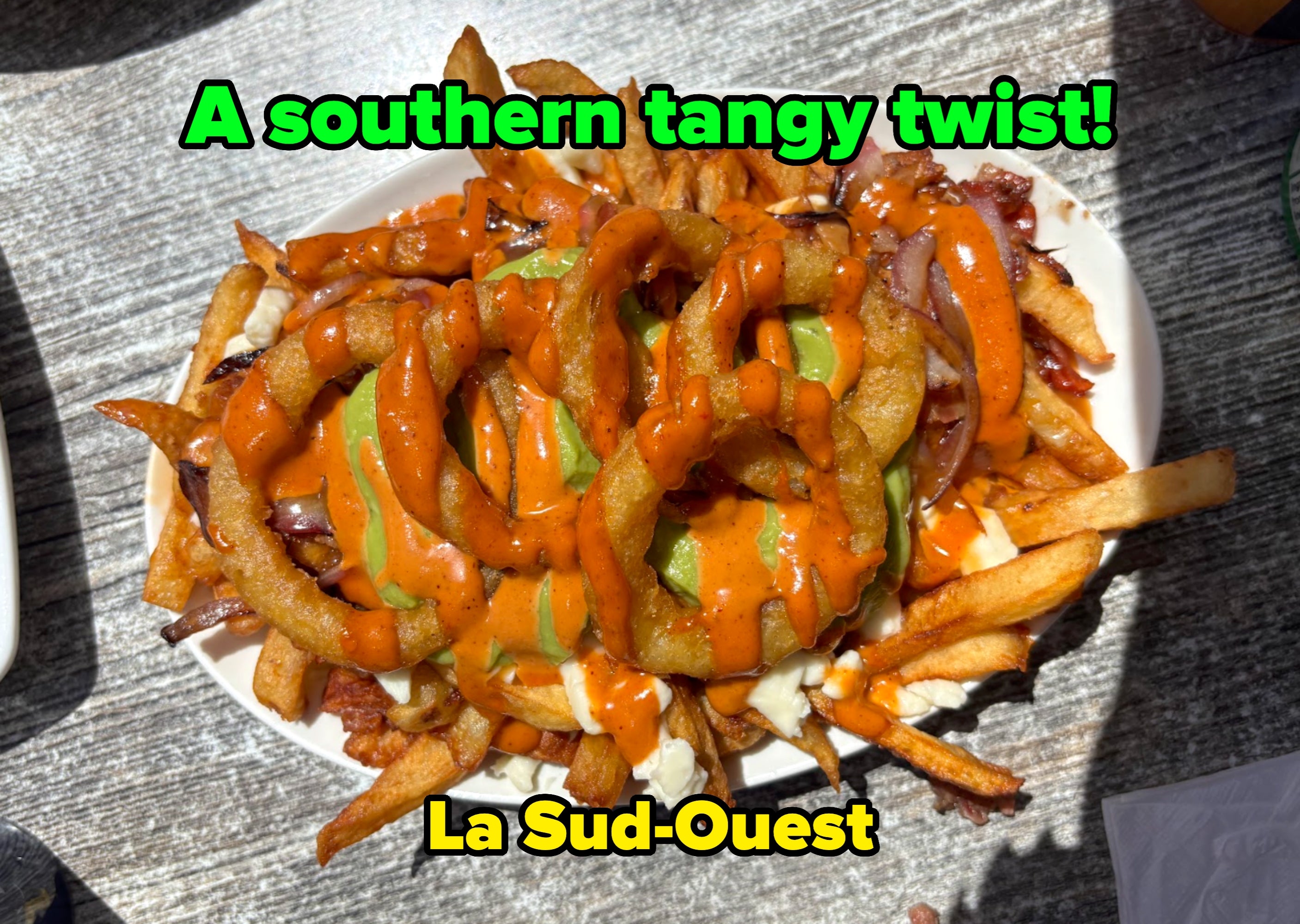 A sheet of fries topped with bulb rings, sauce, and pickles, acceptable connected a woody table