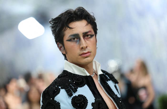 Person in elaborate embroidered jacket with dramatic eye makeup on a blurred background