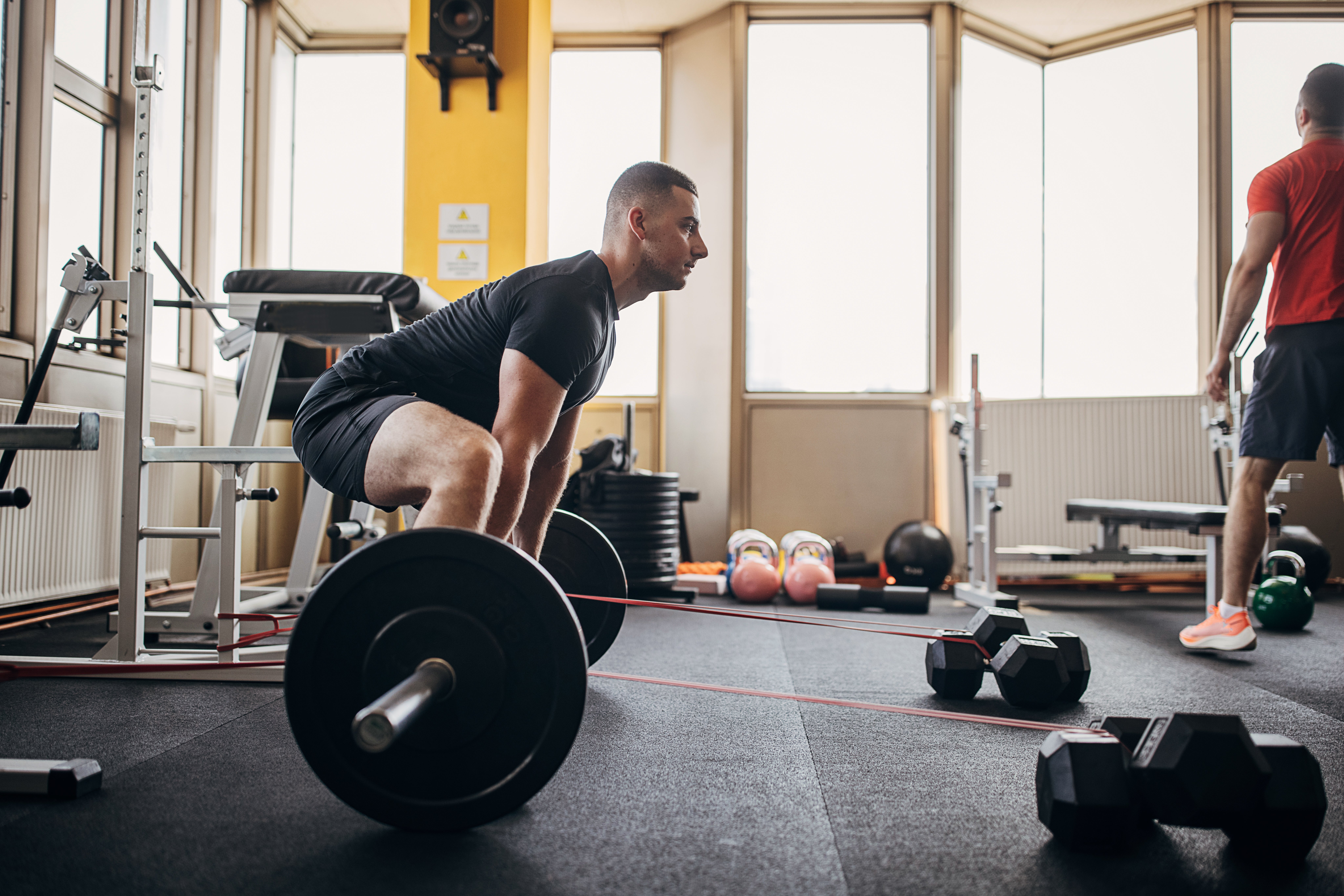 A idiosyncratic successful a gym performs a deadlift with a barbell, focusing connected form. Gym instrumentality and different idiosyncratic are disposable successful the background