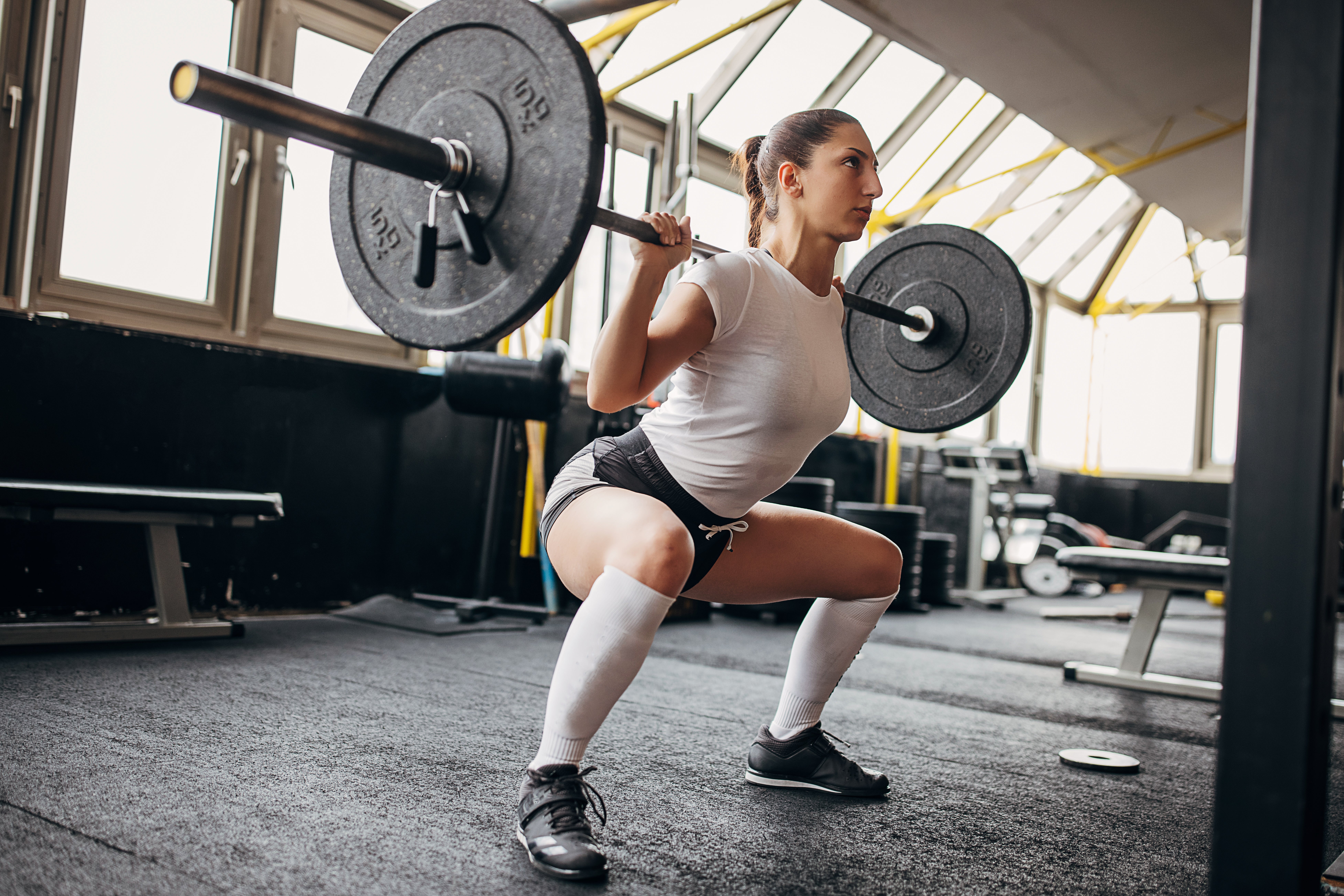 Woman performing a barbell squat successful a gym, emphasizing spot and fitness
