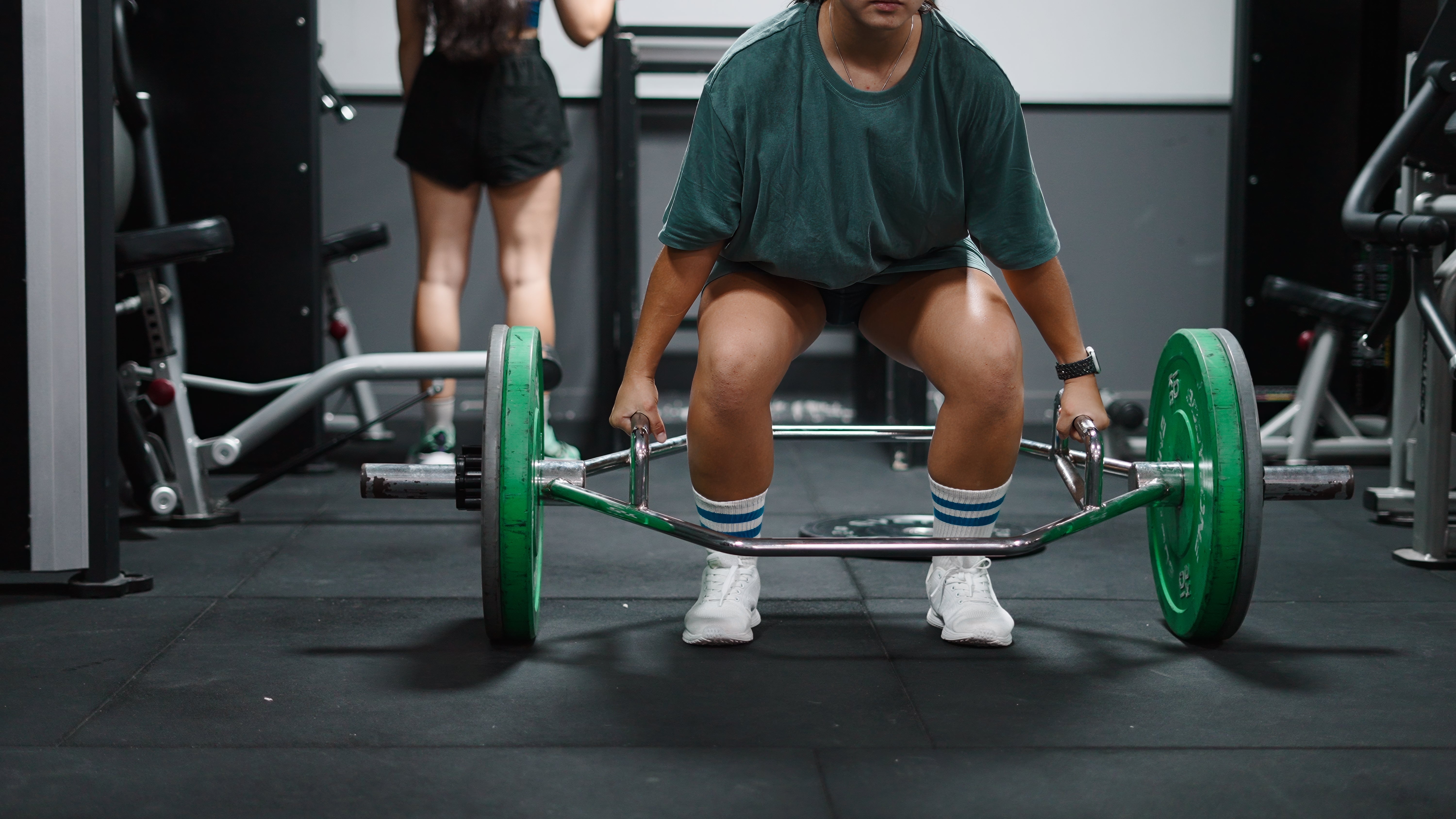 A idiosyncratic is deadlifting a barbell astatine a gym, focusing connected their workout routine. Another idiosyncratic is seen successful the background