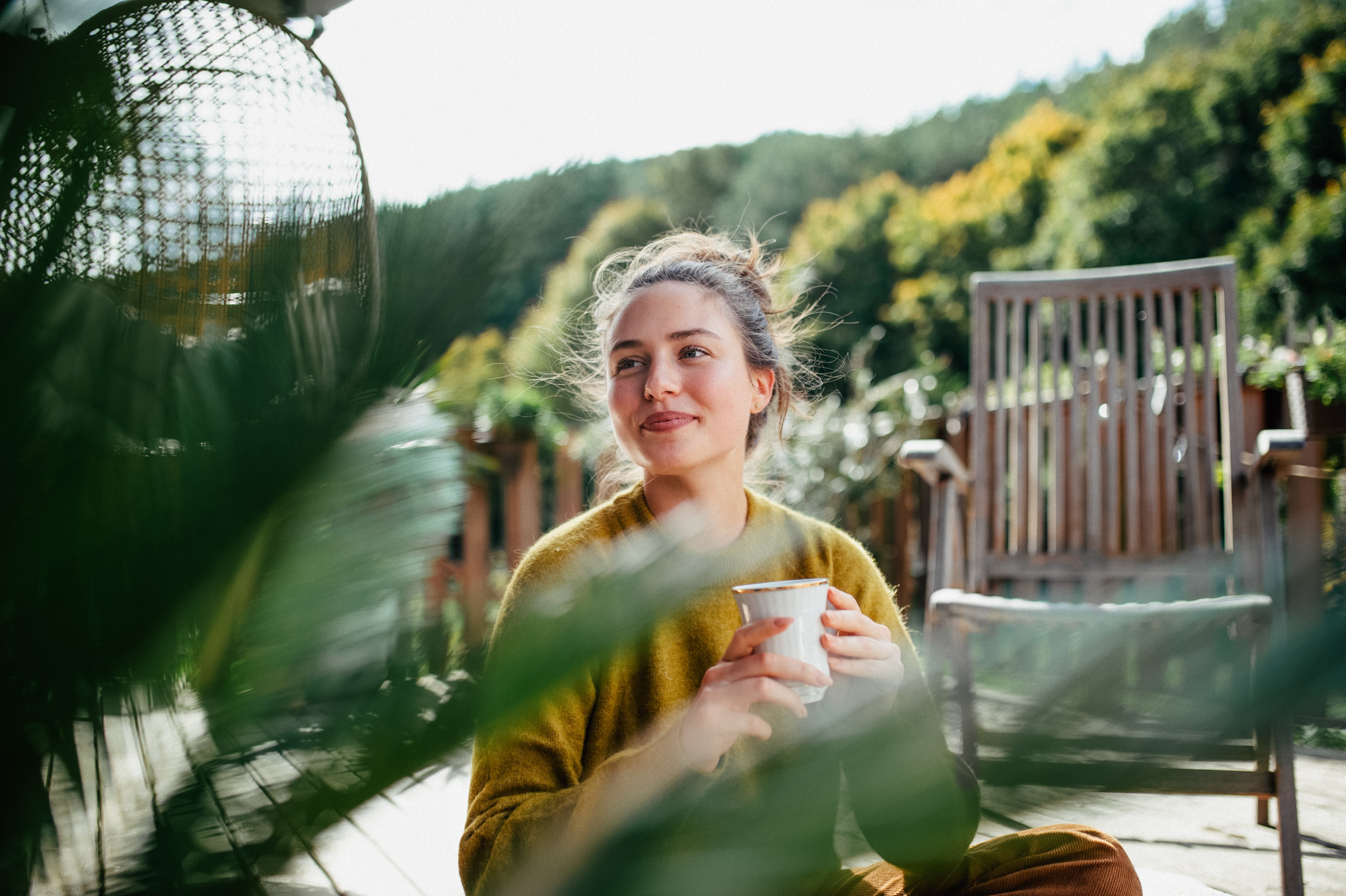 Person outdoors holding a mug, seated amidst greenery and trees, with a relaxed expression