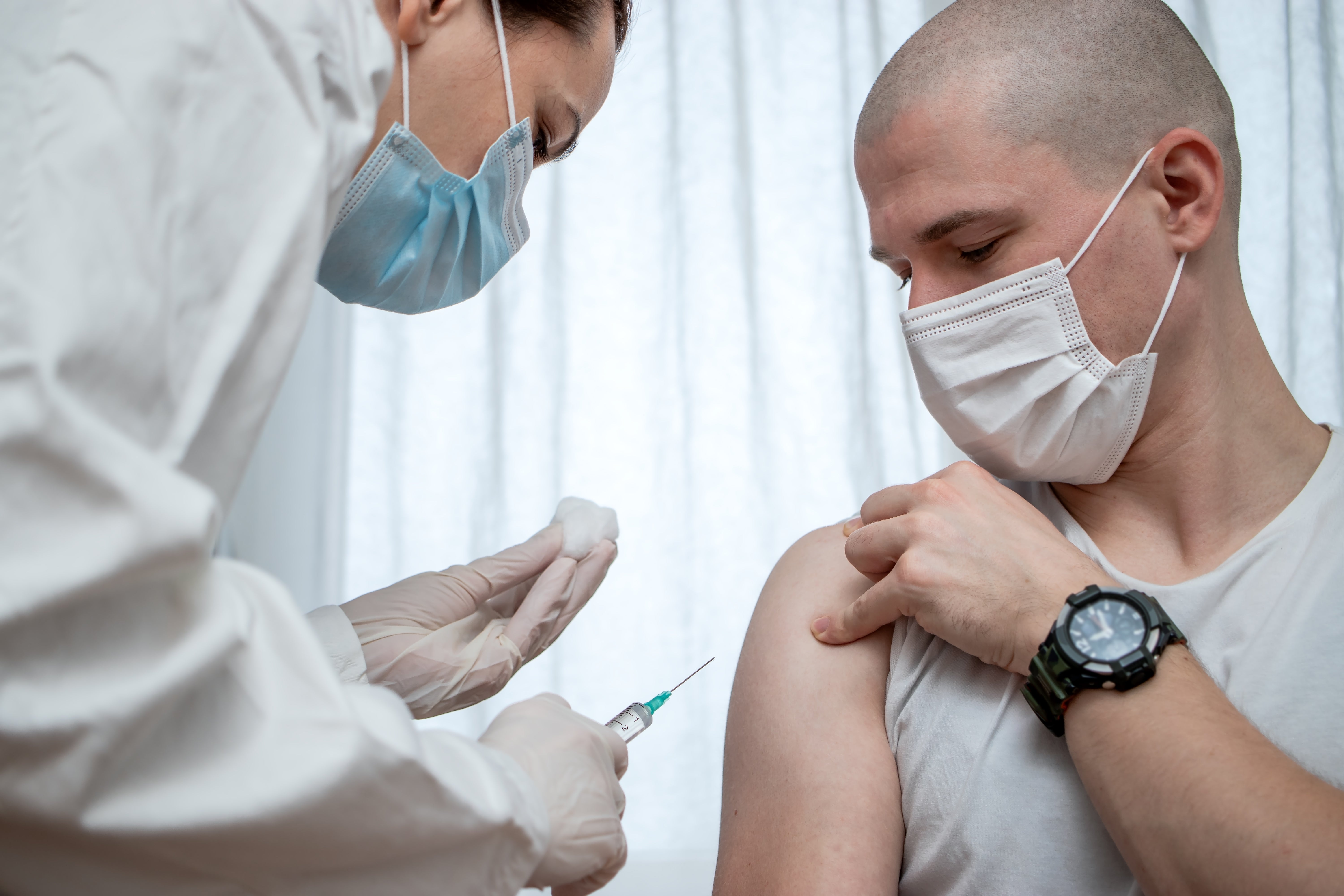 Healthcare nonrecreational  administers a vaccine to a masked person, who looks astatine  the needle portion    holding up   their sleeve