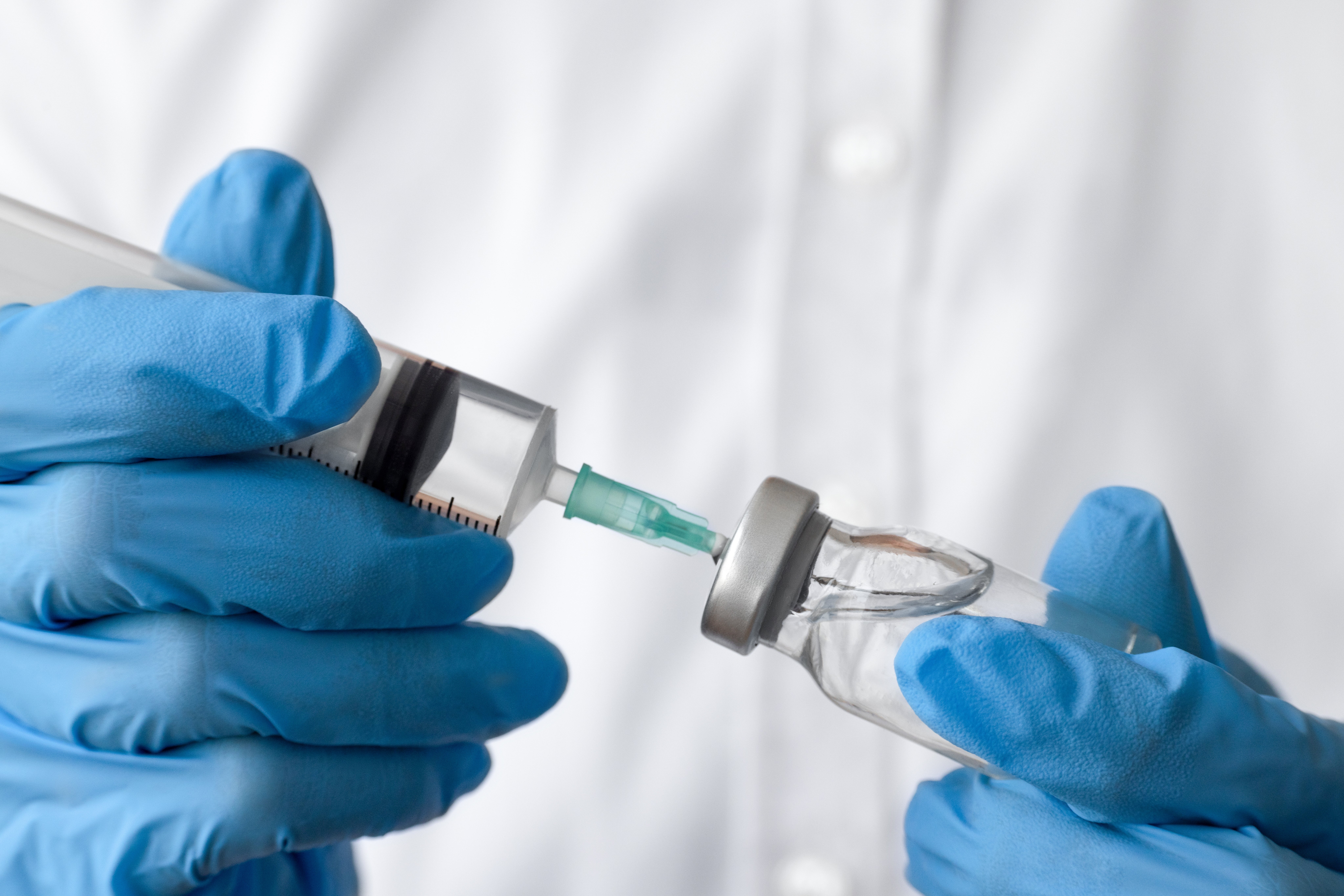 Gloved hands hole   a syringe by drafting  liquid from a vial