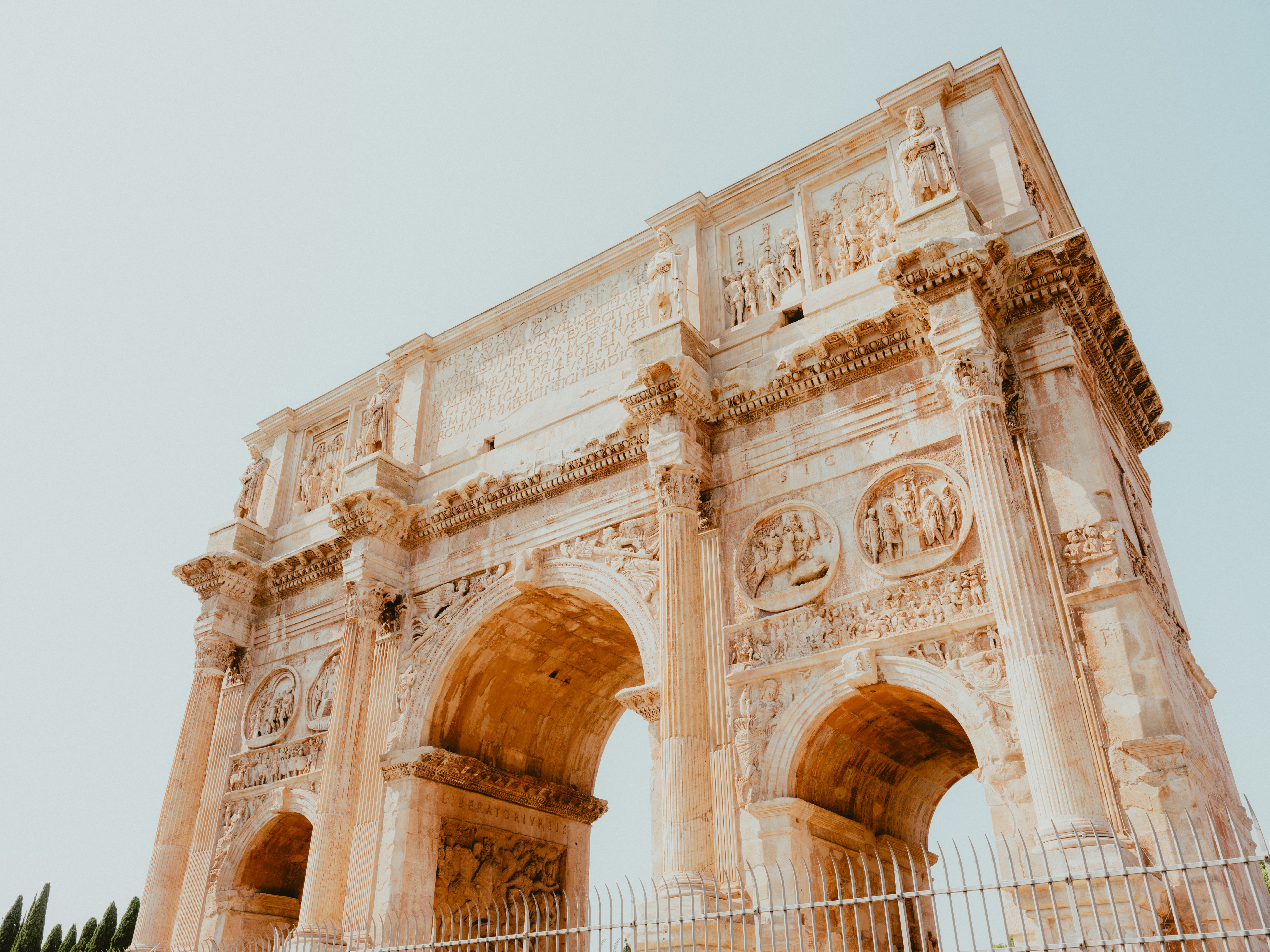Ancient Roman triumphal arch with elaborate carvings, 3 ample arches, and intricate sculptures, viewed from below