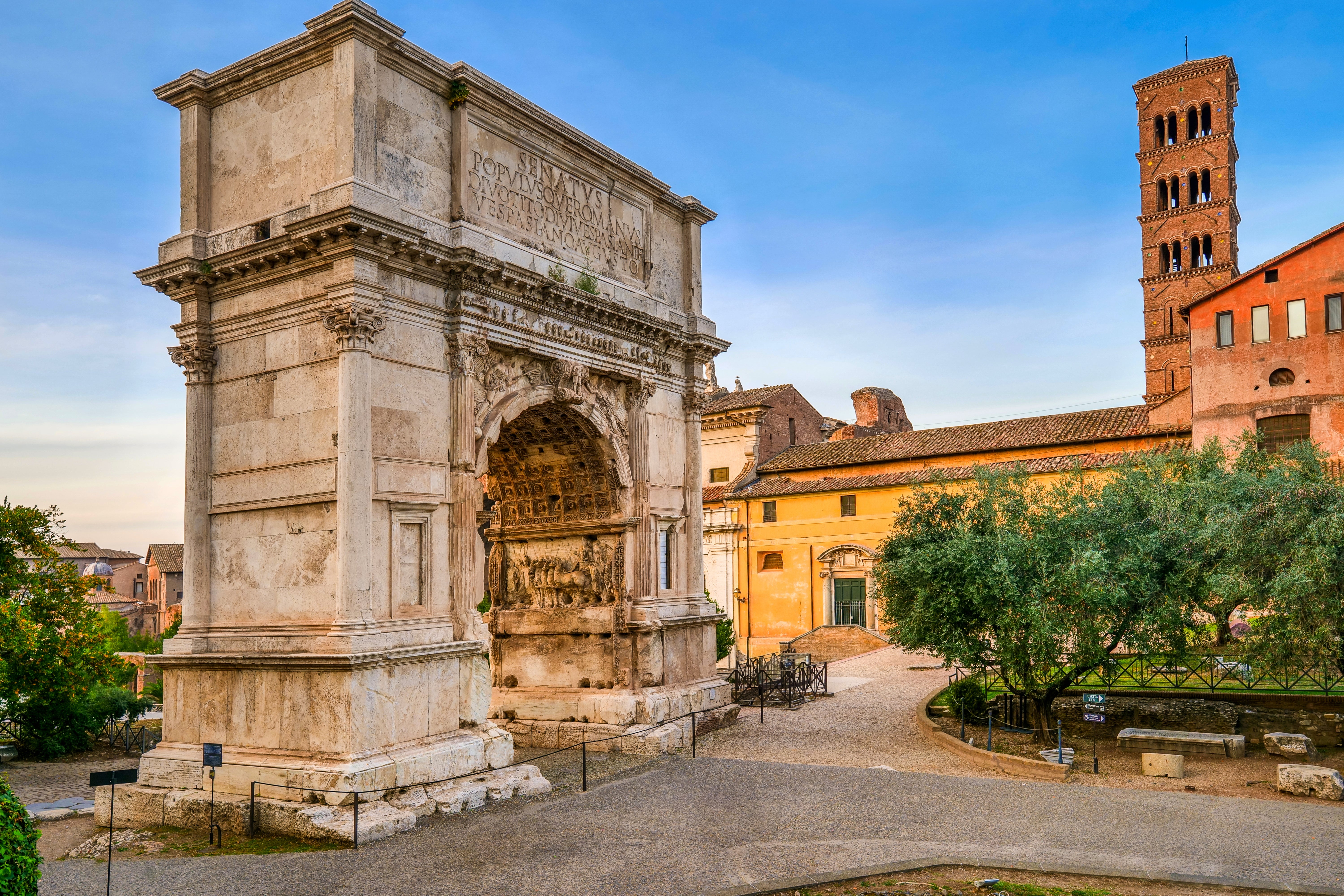 Ancient Roman arch with elaborate carvings, surrounded by historical buildings and trees successful a peaceful setting