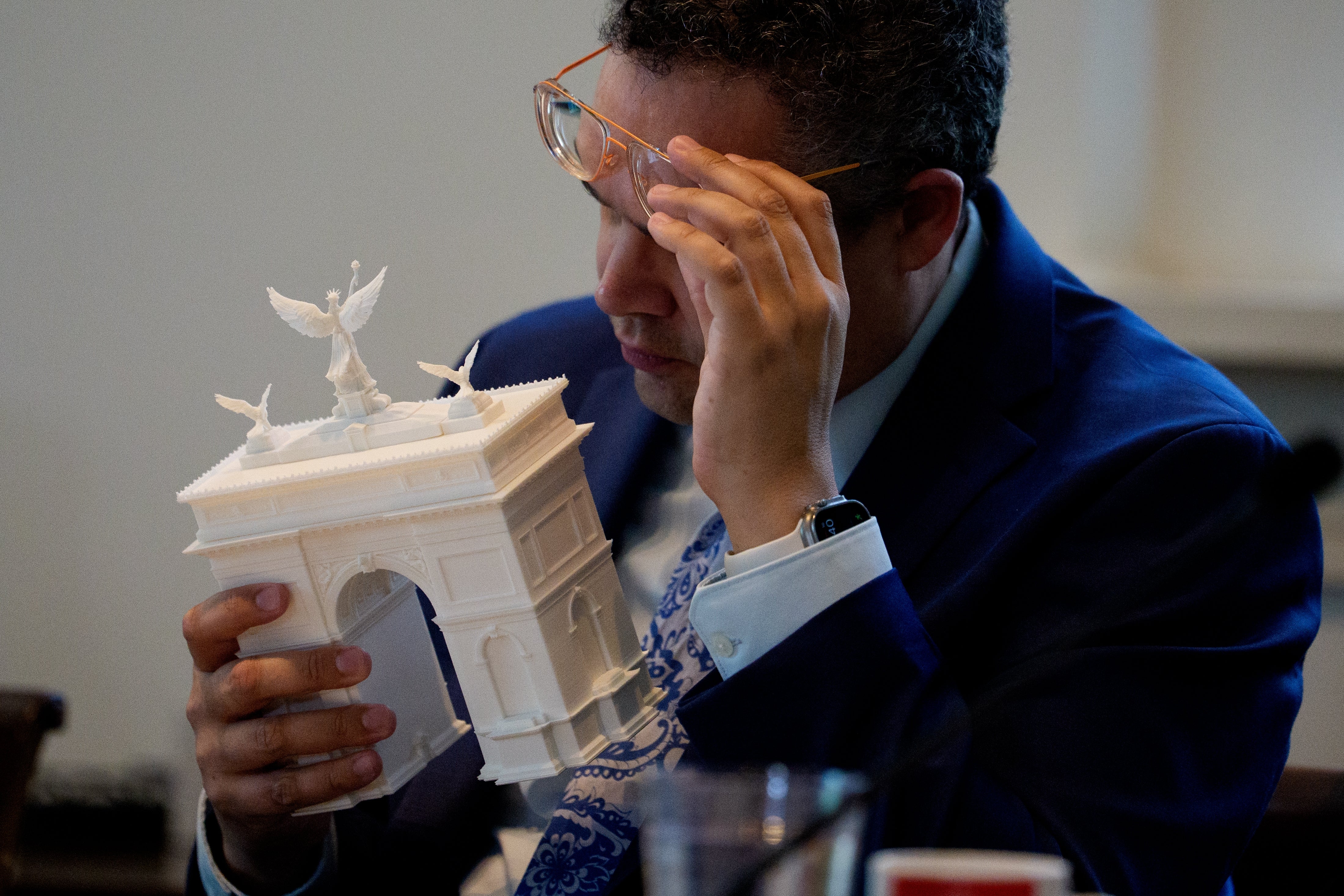 Person successful a suit examines a tiny architectural exemplary of an arch, adjusting their glasses thoughtfully