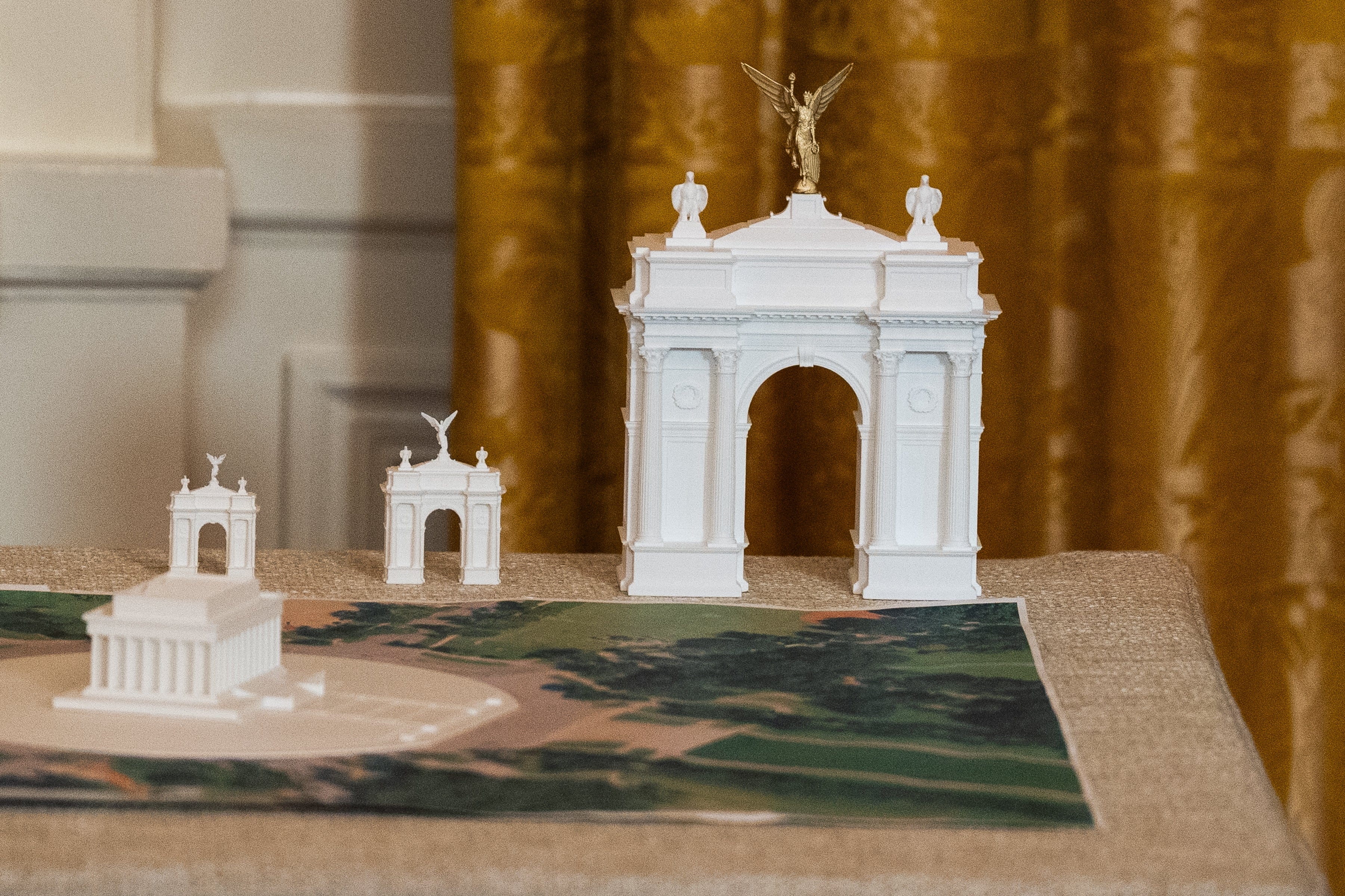 Scale models of architectural structures are displayed connected a table, including an arch and a building, suggesting a readying oregon plan presentation