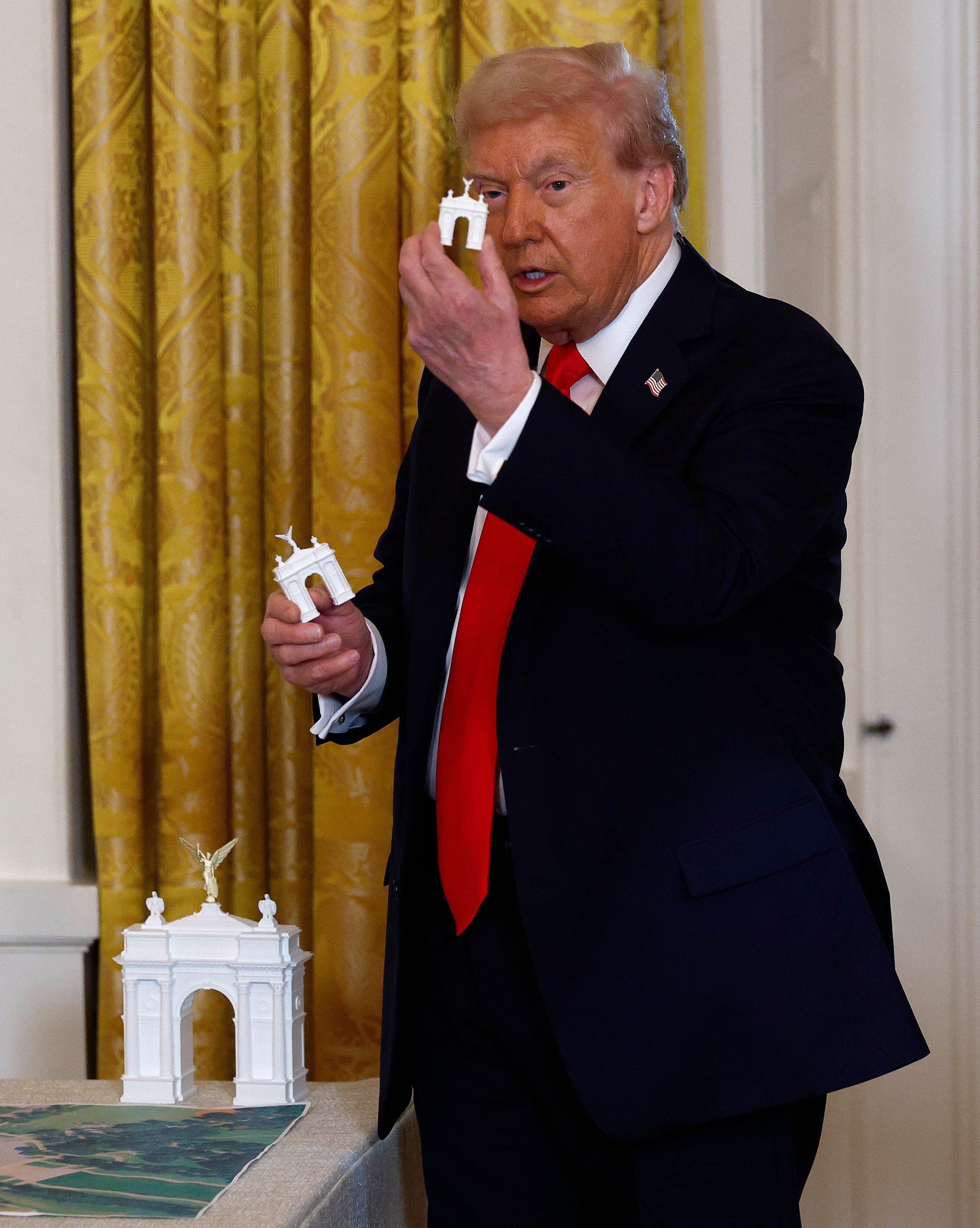 A idiosyncratic successful a suit holds a tiny exemplary of a monument, lasting adjacent a larger exemplary connected a table, appearing engaged successful a presumption oregon discussion
