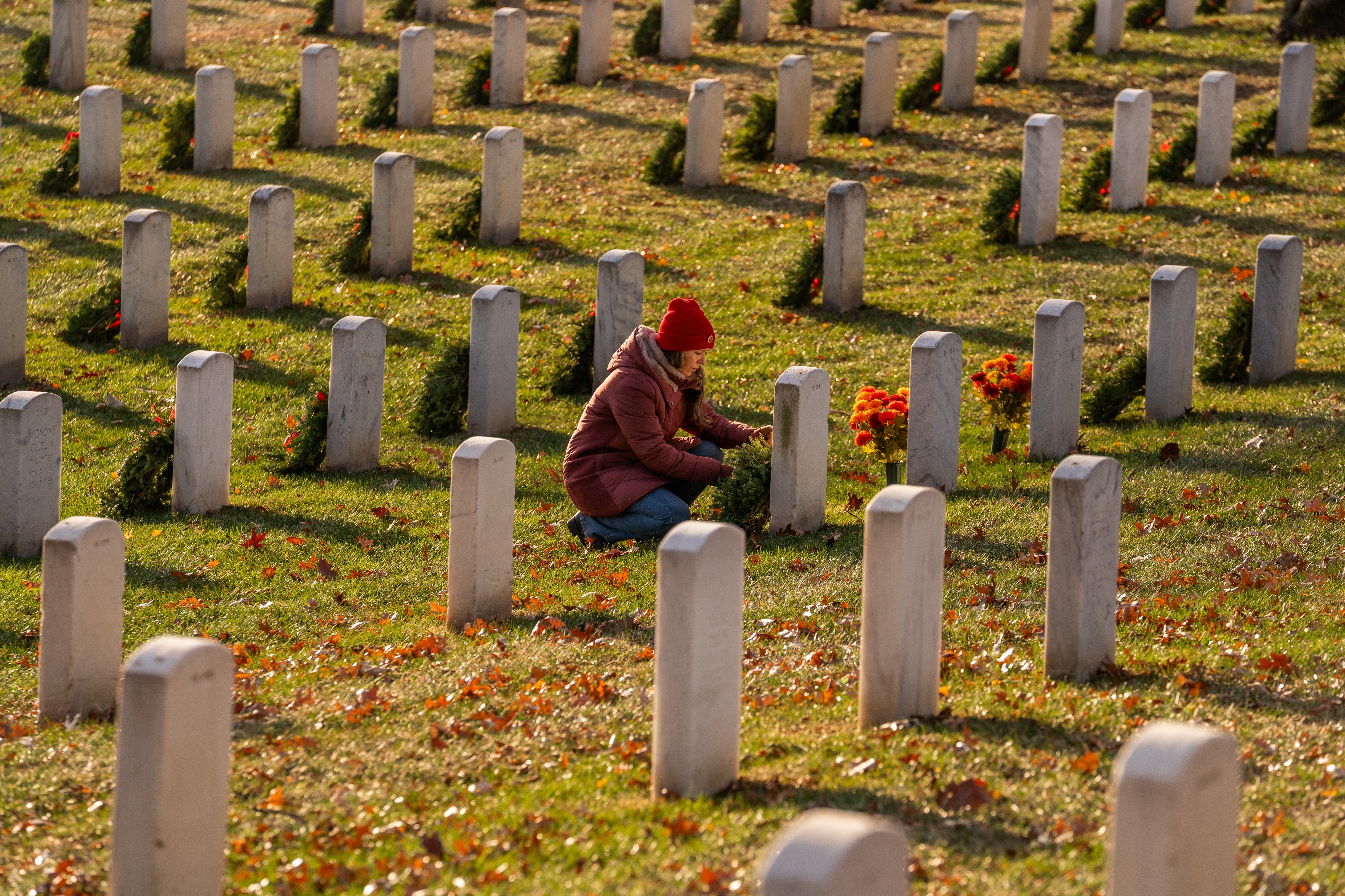A idiosyncratic successful a reddish chapeau places flowers astatine a gravestone successful a cemetery, surrounded by rows of headstones