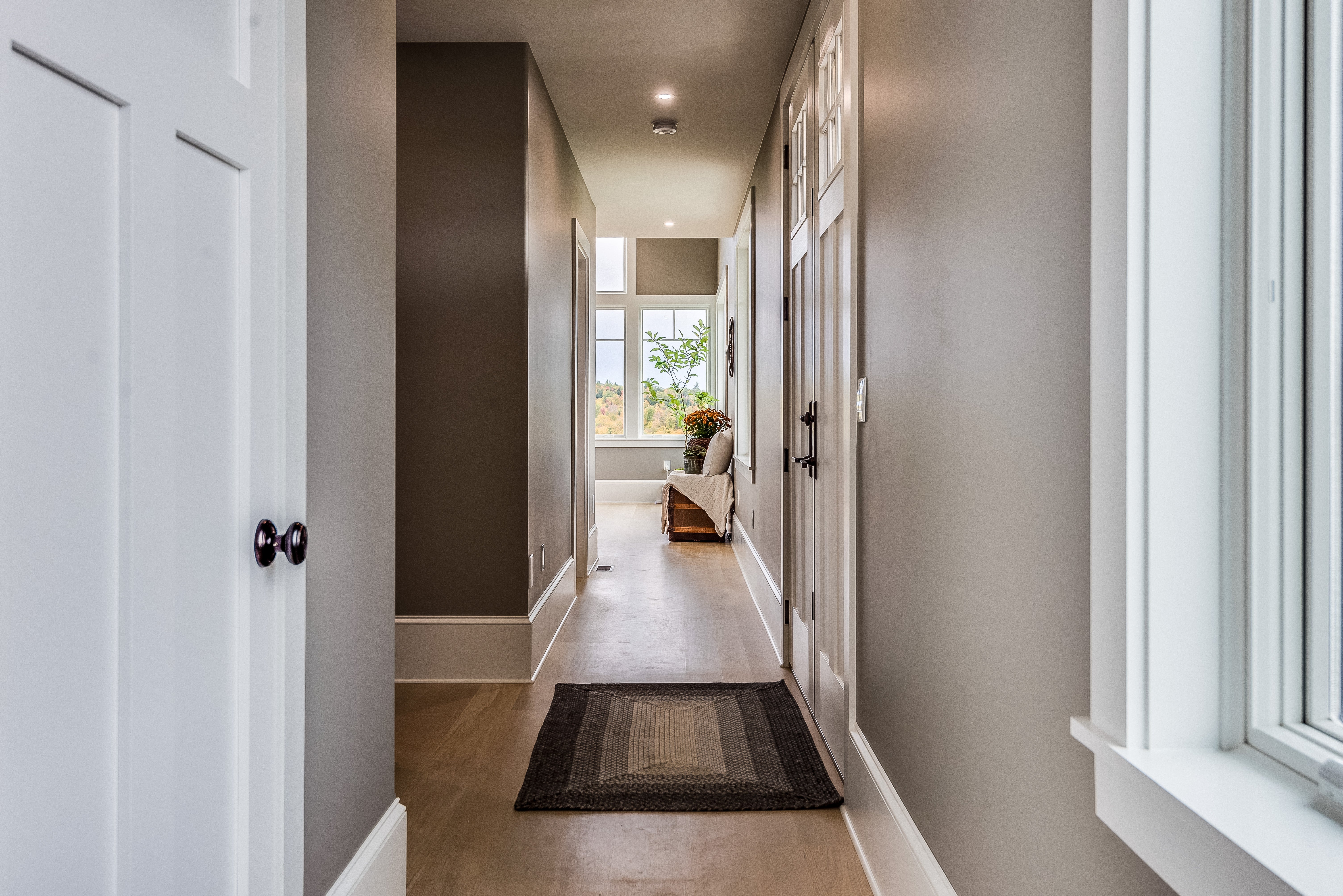 Hallway with woody flooring, neutral-toned walls, and a model astatine the extremity letting successful earthy light; a seat is disposable adjacent the window