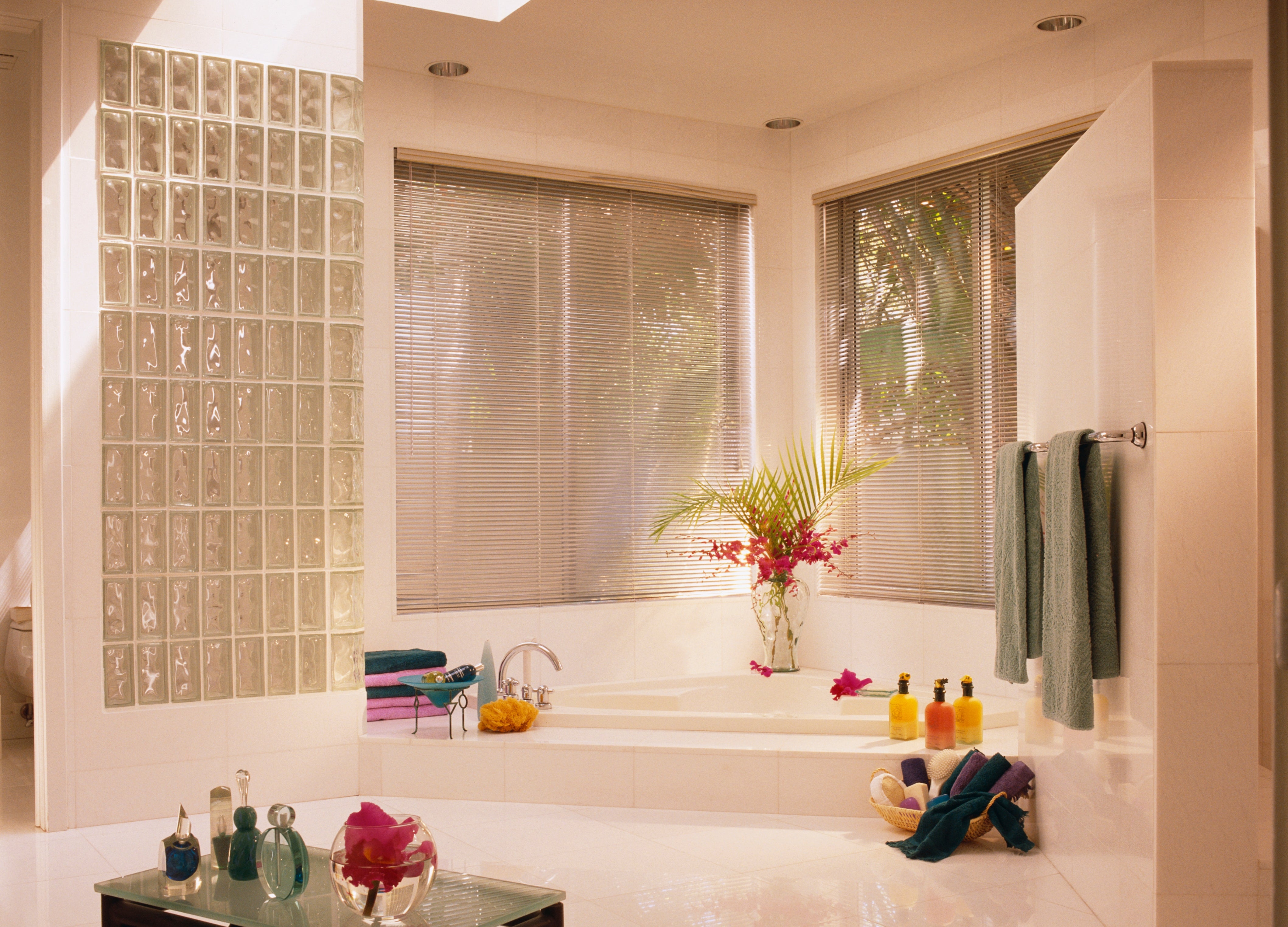 Luxurious bath with ample windows, solid artifact wall, sunken tub, colorful towels, and a tiny array with toiletries
