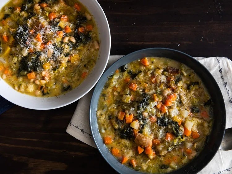 Two bowls of hearty vegetable soup with chunks of carrots, greens, and cheese on a wooden table