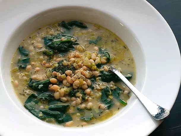 A bowl of soup with beans, greens, and a broth, served with a spoon