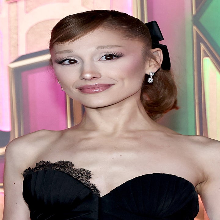 Person in elegant black strapless dress with lace detail, attending an event. Background features decorative, colorful lettering