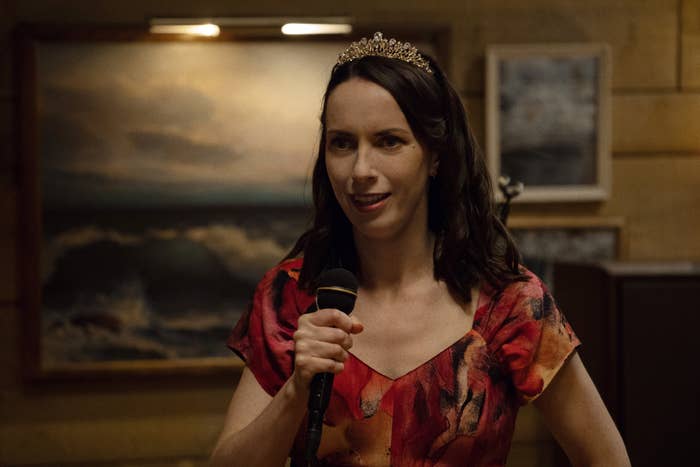 A idiosyncratic   wearing a decorative headband and patterned formal  speaks into a microphone successful  a country   with paintings connected  the wall