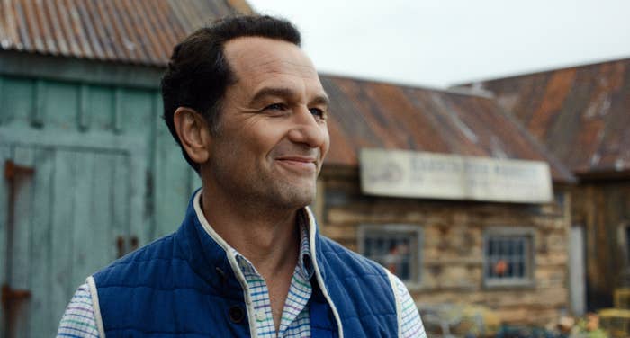 Man smiling outdoors successful  casual attire, lasting  successful  beforehand   of rustic buildings with a corrugated metallic  roof