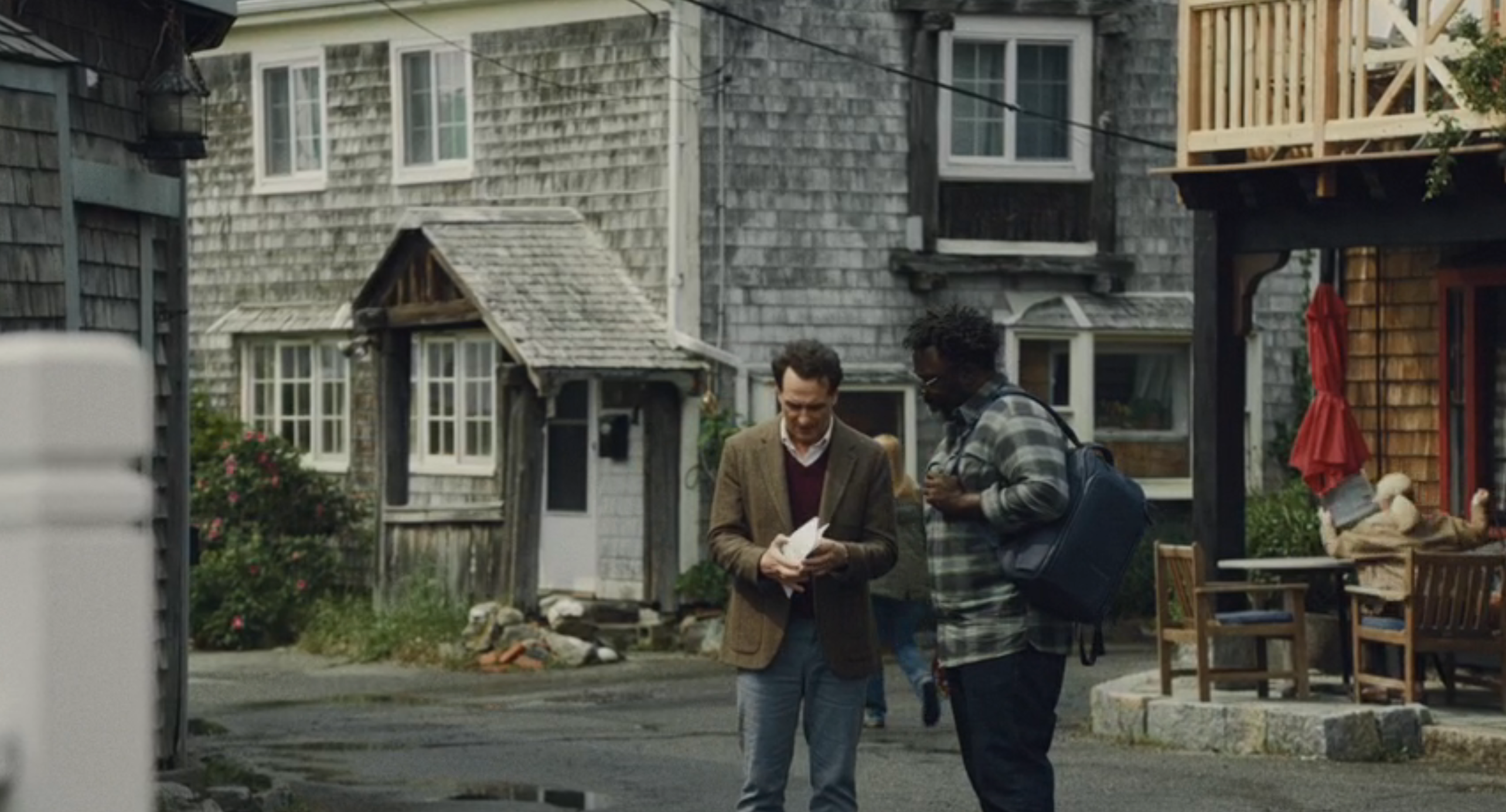 Two radical   casually walking and talking connected  a quaint thoroughfare  with rustic buildings and outdoor seating