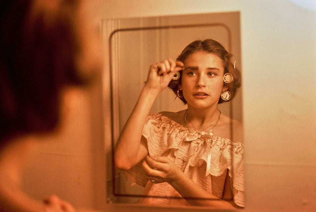 Anak muda menggunakan rol rambut dan melihat ke cermin, mengenakan atasan off-shoulder