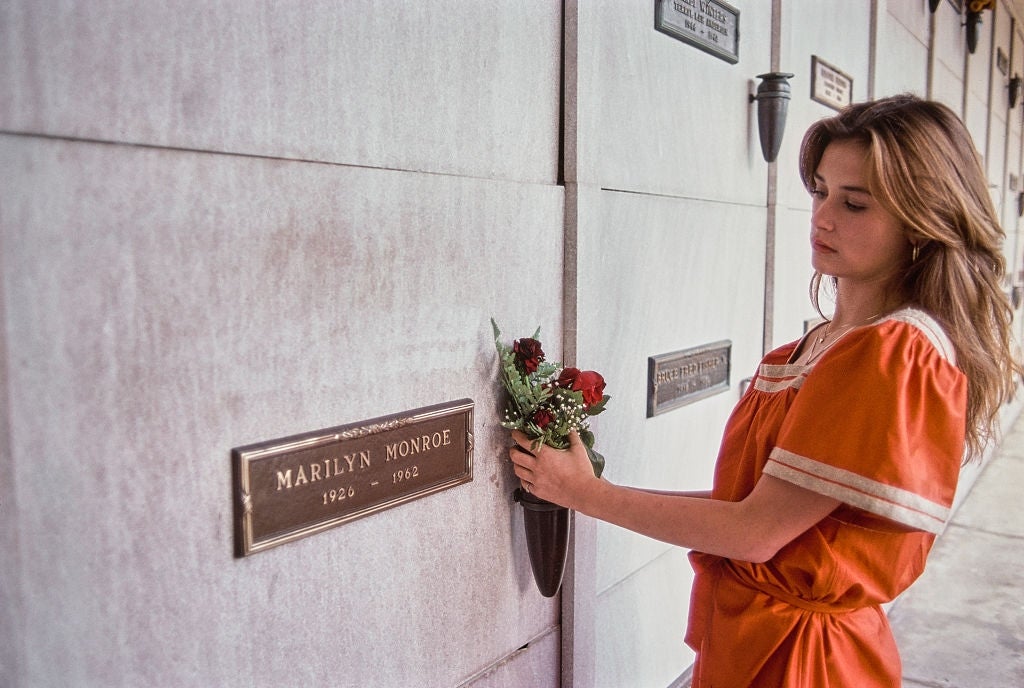 Seseorang dengan pakaian kasual meletakkan bunga di plakat peringatan Marilyn Monroe