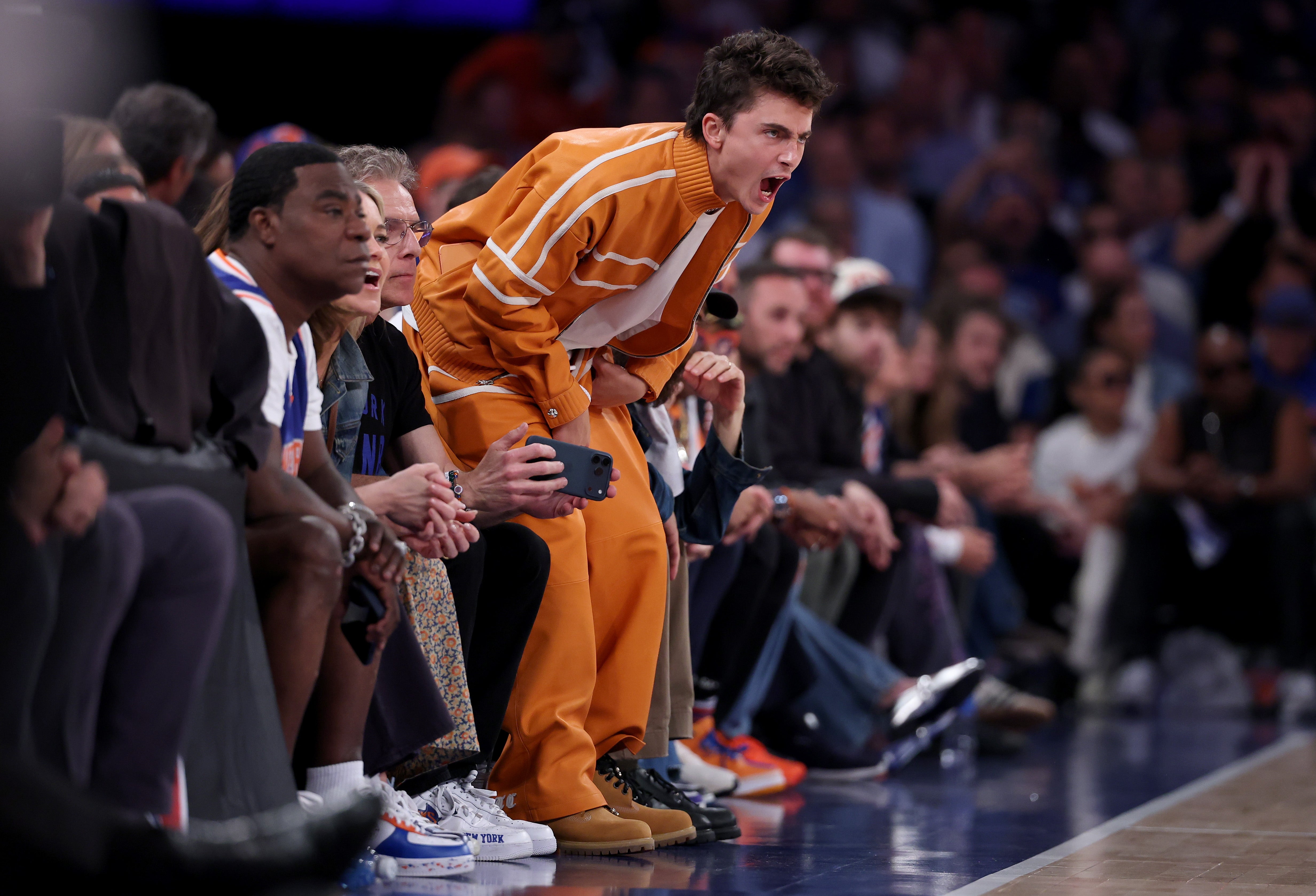 Person successful  a casual diversion  tracksuit cheers enthusiastically from the beforehand   enactment      astatine  a sports event, surrounded by different   spectators