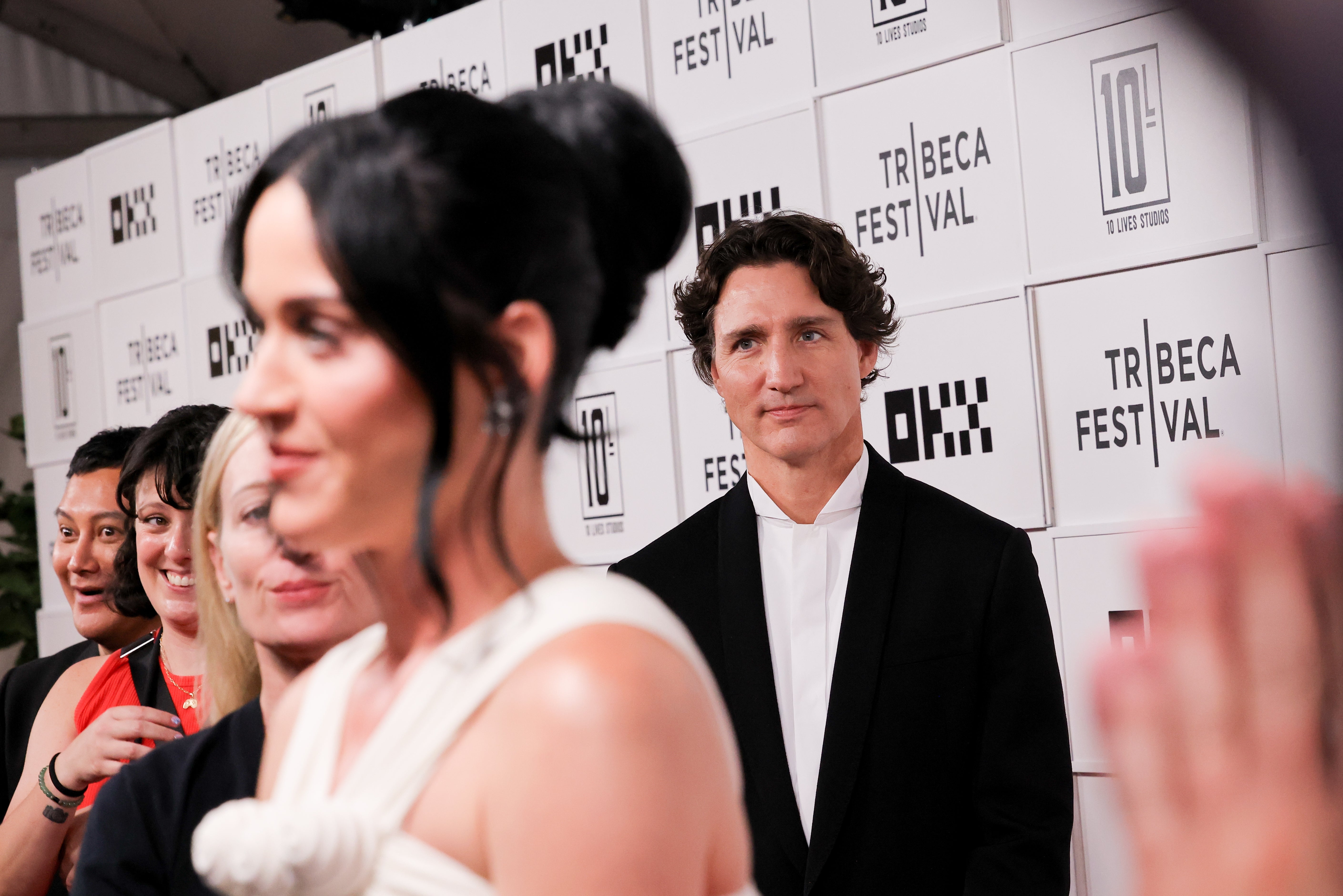 A personage successful a ceremonial achromatic suit stands connected the Tribeca Festival reddish carpet, looking towards different guests