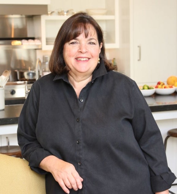 Person smiling successful  a kitchen, wearing a simple-collared shirt. Kitchen has neatly arranged utensils and a vessel  of effect   successful  the background