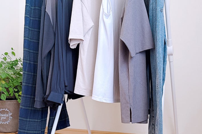 洋服ラックにシャツやジーンズがかけられており、部屋の一角に植物が置かれている。