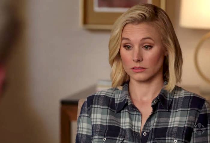 Person with medium-length hairsbreadth  sits indoors, wearing a plaid shirt, looking thoughtful