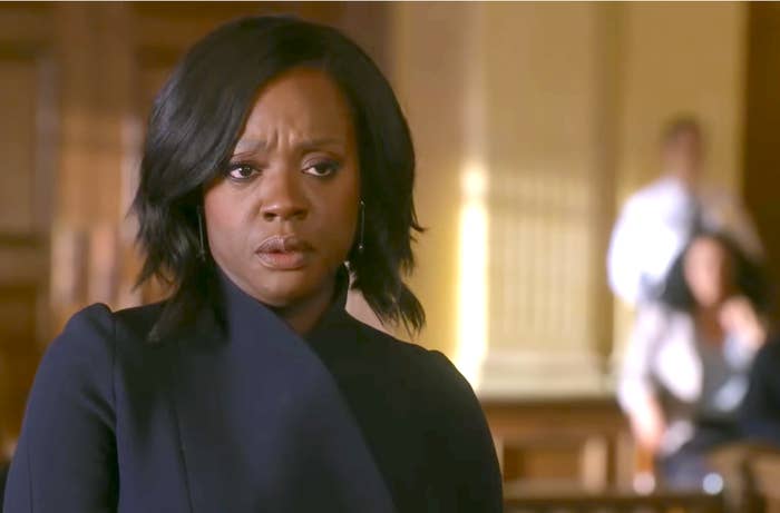 Person successful  a courtroom setting, wearing a stylish acheronian  outfit, appears concerned. Background shows blurred figures, suggesting a tense ineligible  scenario