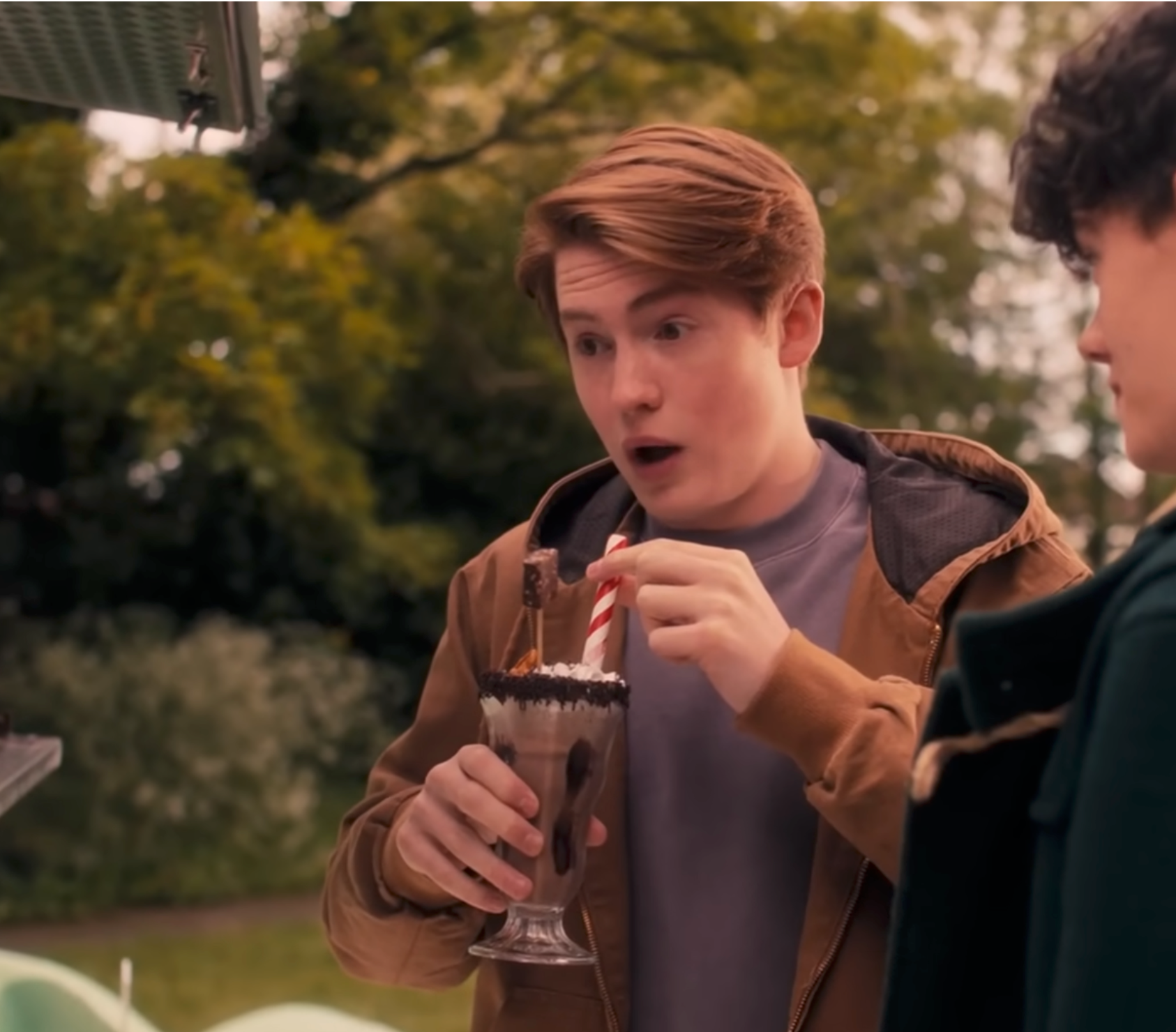 Person looks amazed portion holding a milkshake outdoors adjacent to different person