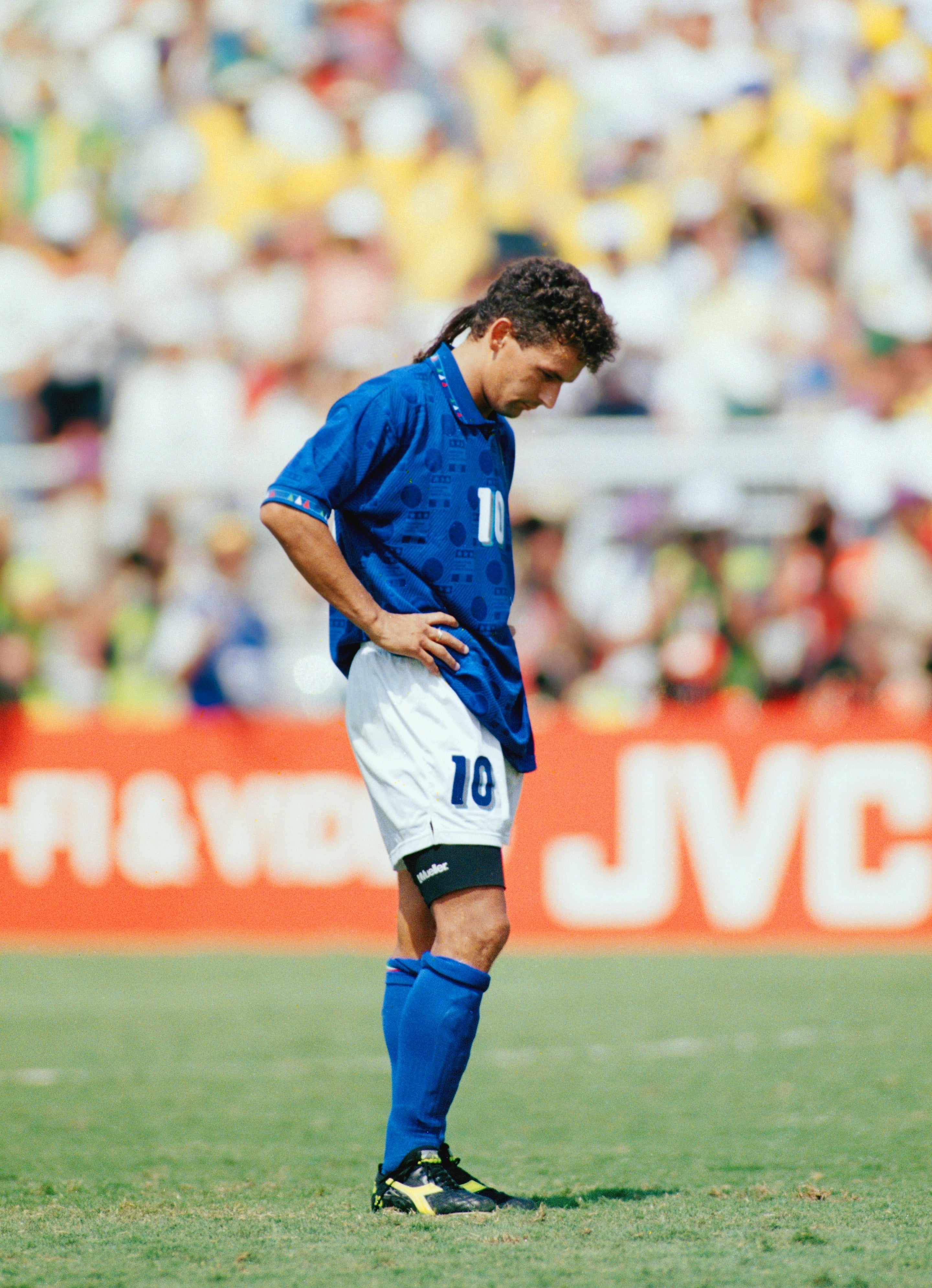 Soccer subordinate successful a bluish jersey and shorts looks down connected the tract during a game, appearing contemplative oregon disappointed