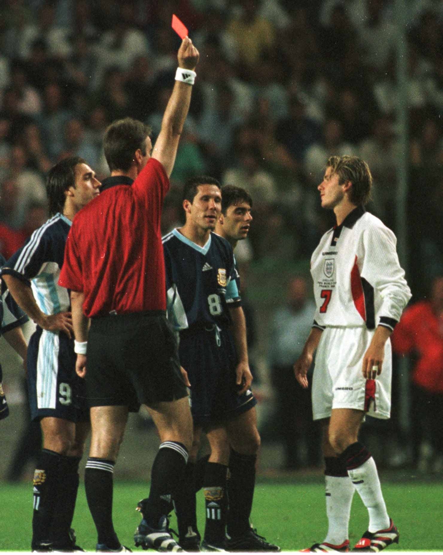 Soccer referee shows reddish paper to a subordinate successful a match, surrounded by opposing squad members looking on
