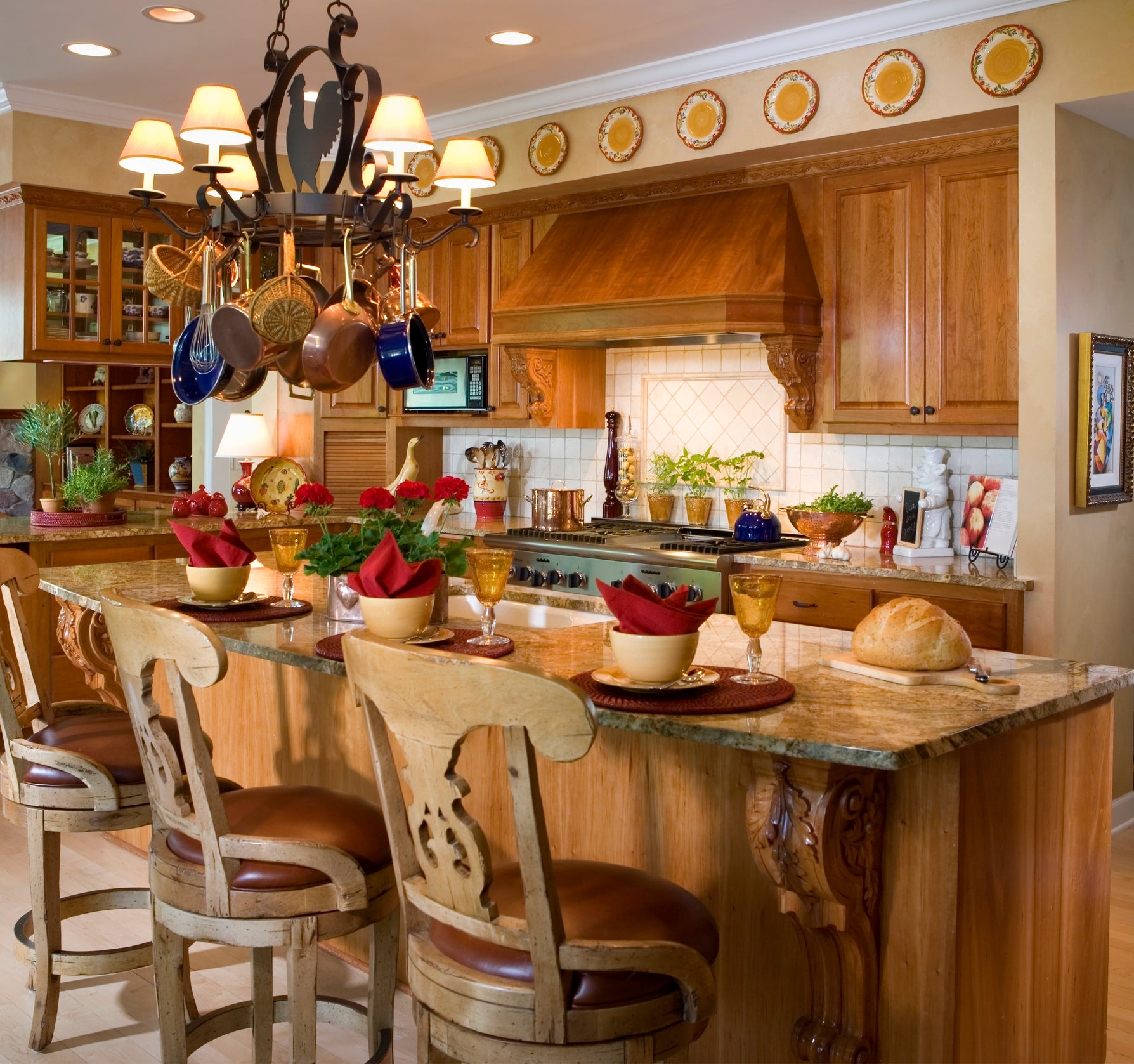 A warm, cozy room with a marble-topped island, woody chairs, and decorative pots hanging from a chandelier, acceptable for eating with reddish napkins